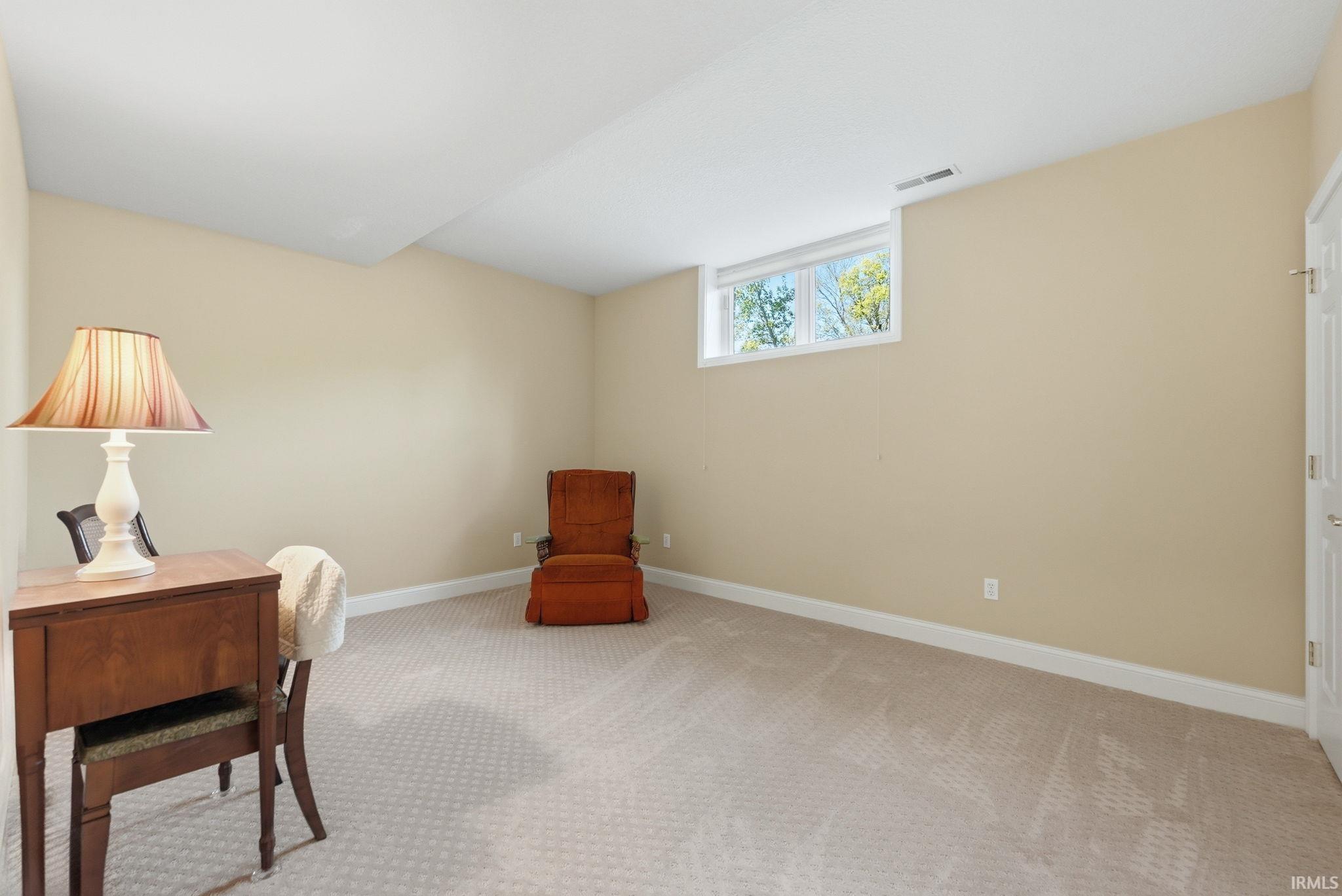 Spacious room featuring neutral wall paint, light-colored patterned carpeting, white trim, and a high window providing natural illumination