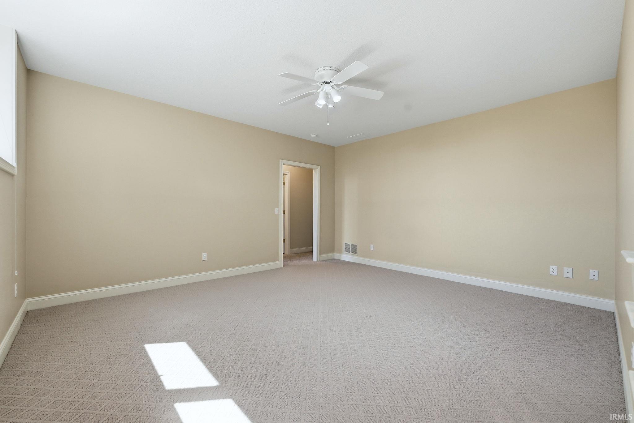 Spacious room featuring patterned carpeting, neutral wall finishes, white trim, and a ceiling fan with integrated lighting