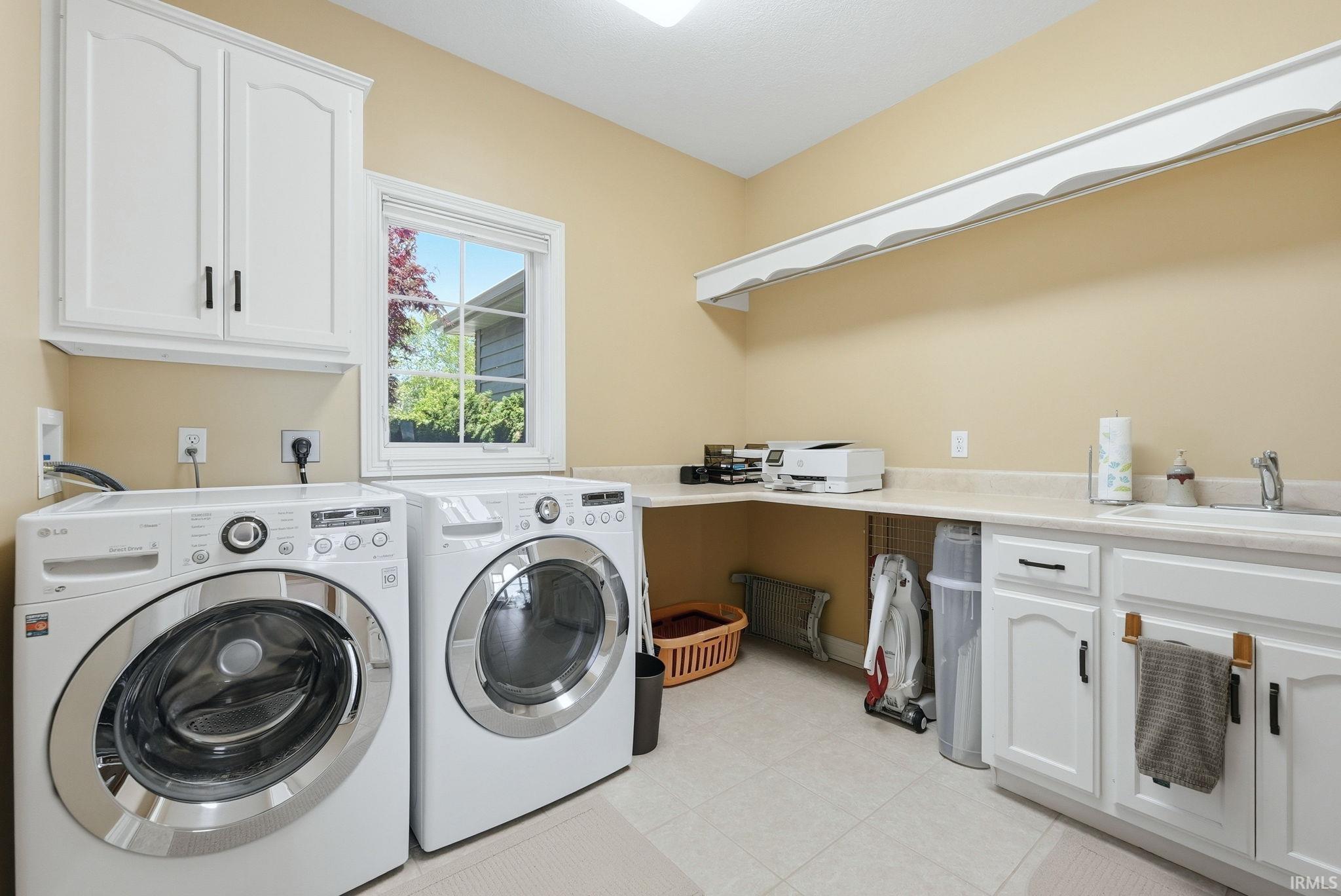 Laundry room featuring light-colored flooring, window, white cabinetry with dark hardware, and a countertop with integrated sink