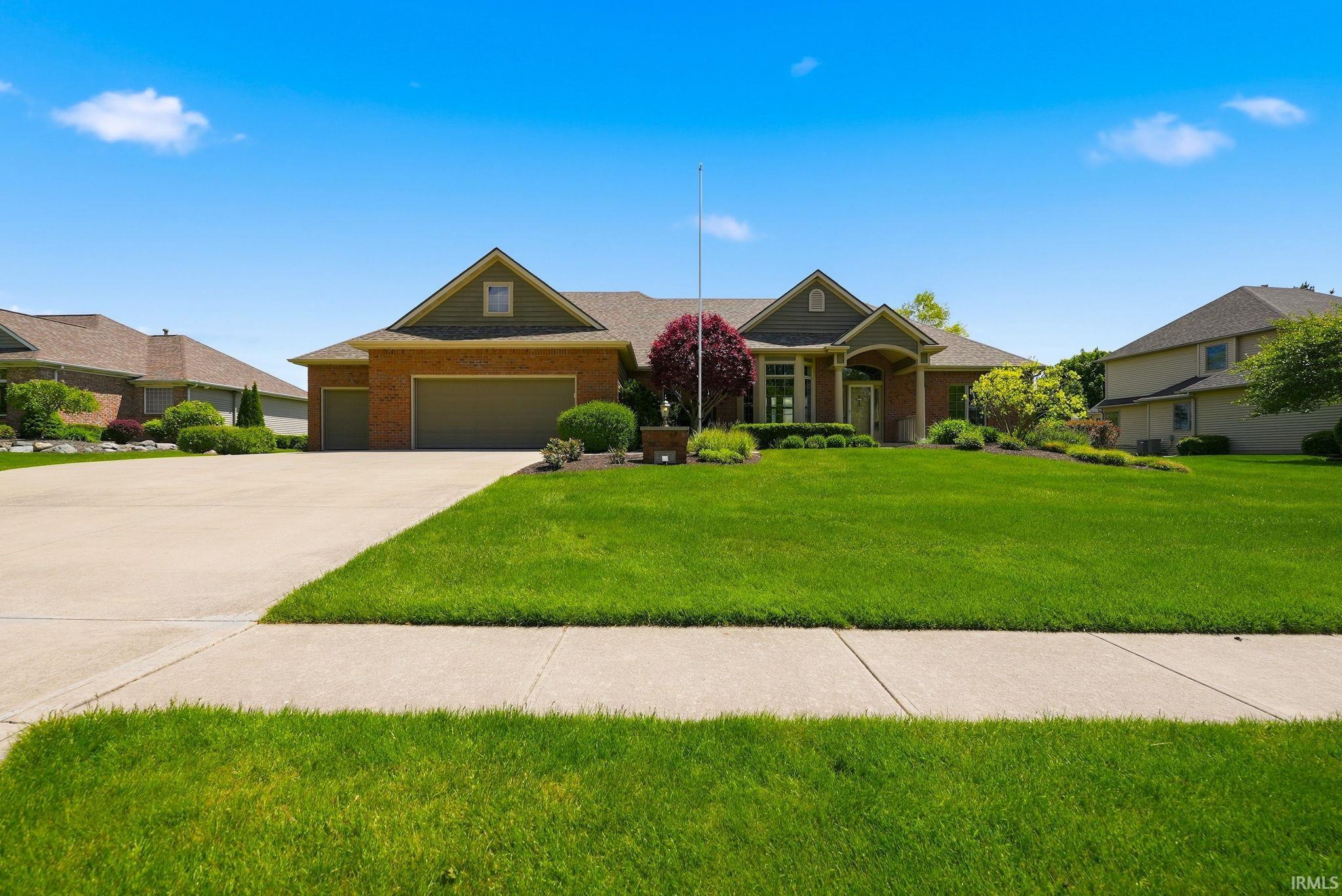 Brick and siding exterior featuring a covered entry porch, an attached garage, a concrete driveway, and established landscaping