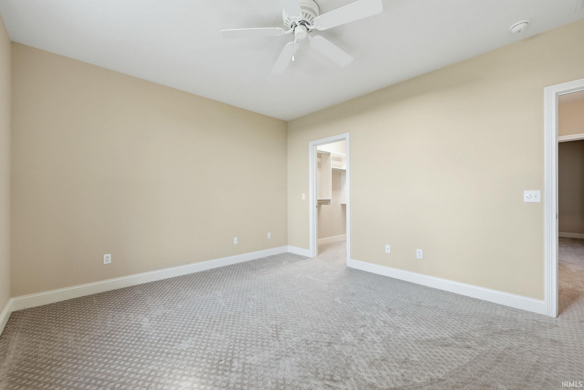 Neutral-toned room featuring a patterned gray carpet, white baseboards, and a ceiling fan with integrated lighting