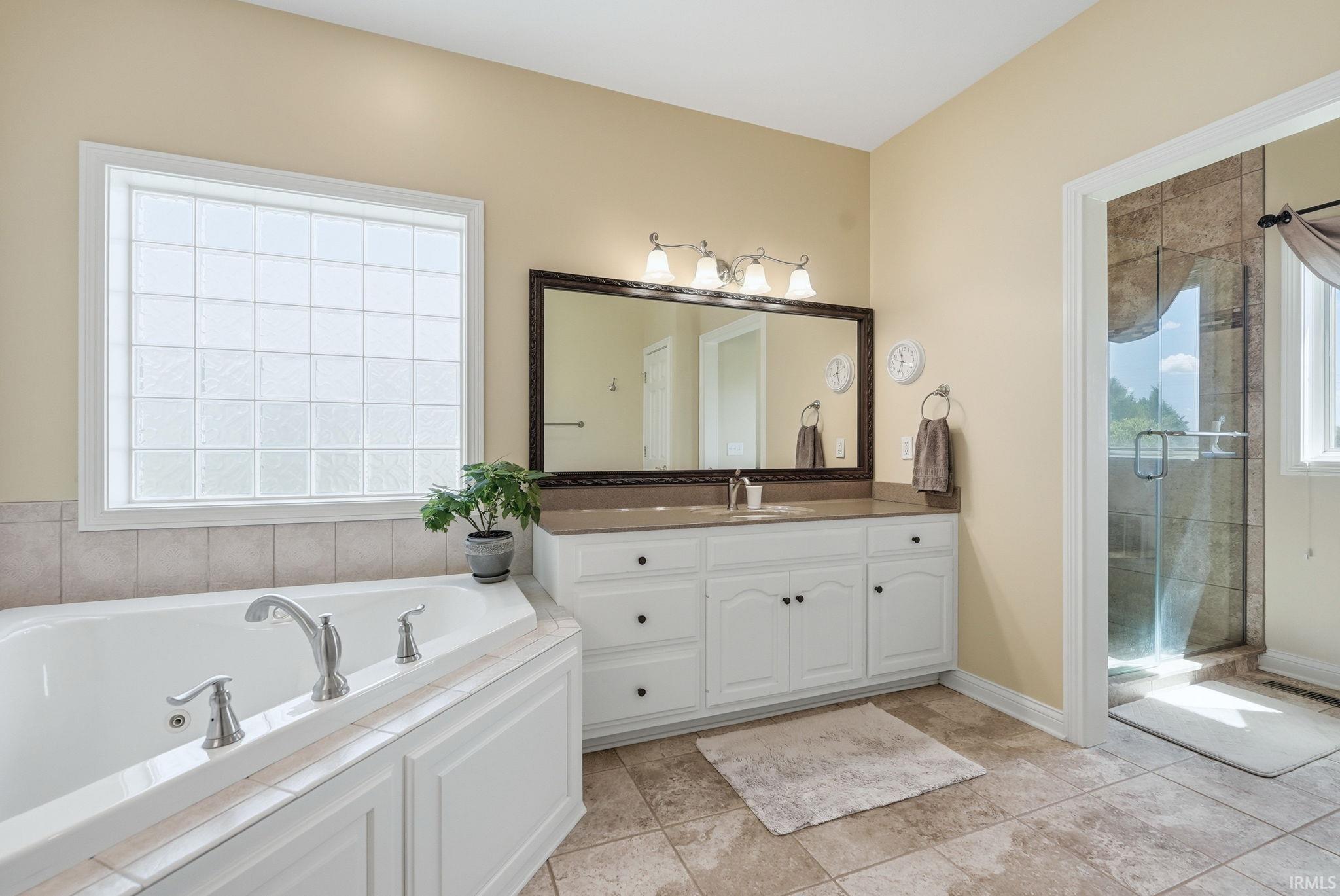 Spacious bathroom featuring a corner soaking tub, glass block window, and a vanity with an integrated sink and large framed mirror