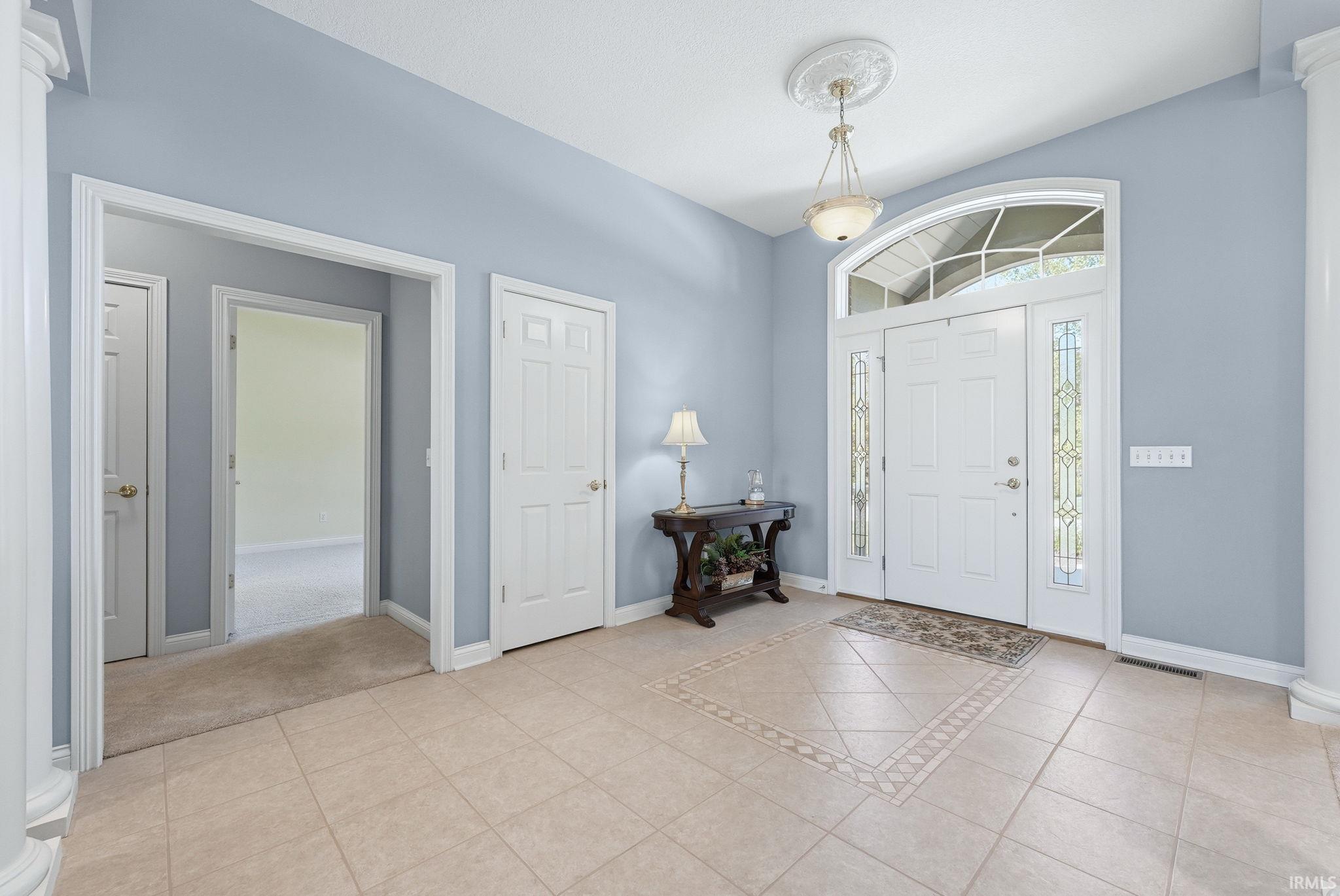 Gracious entryway featuring a decorative light fixture, arched transom window, leaded glass sidelights, and tile flooring with an inlaid design