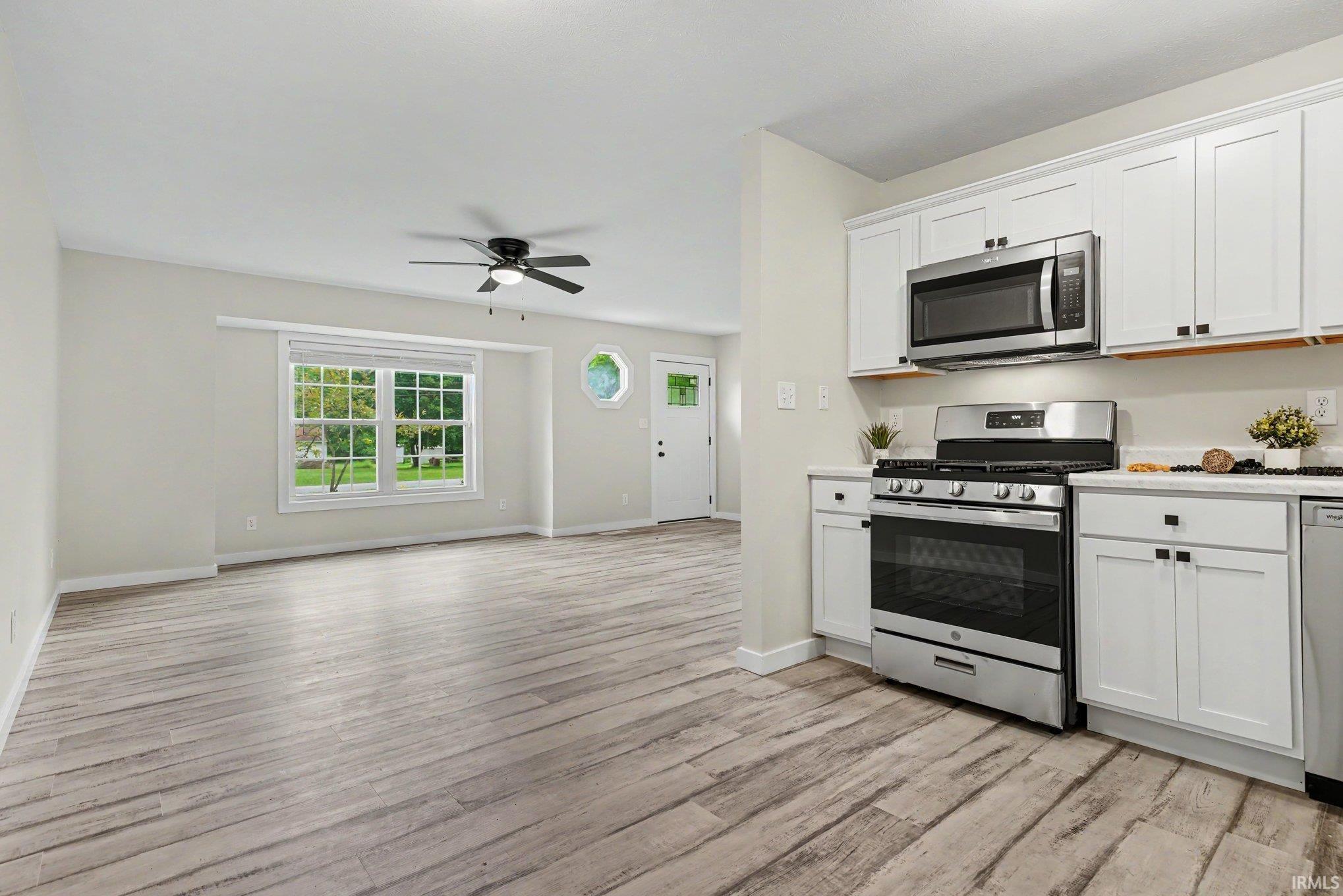 Open-concept living area featuring wood-finish flooring, a contemporary ceiling fan, and a large window