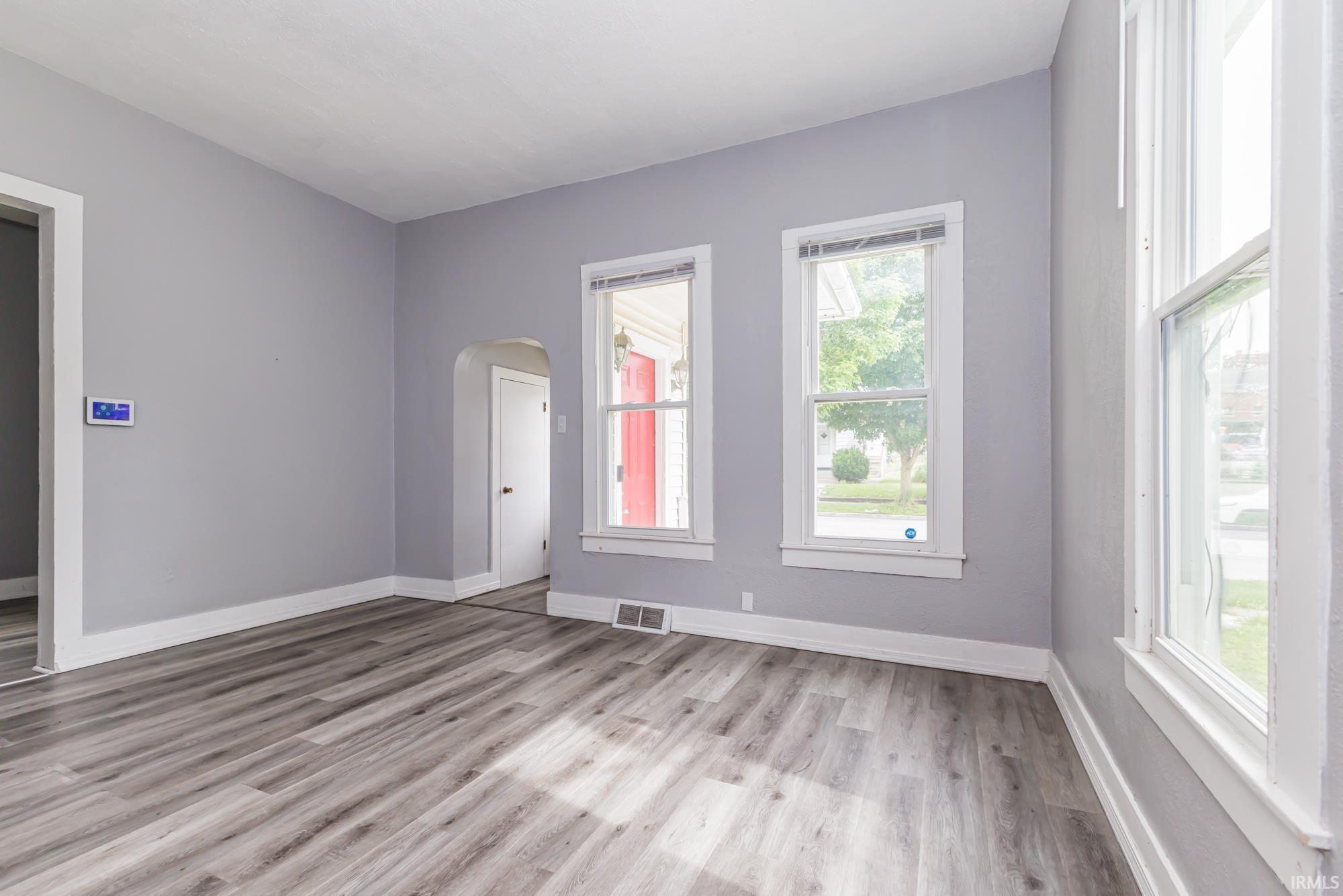 Spacious interior featuring wood-finish flooring, light grey painted walls, white trim, and multiple windows