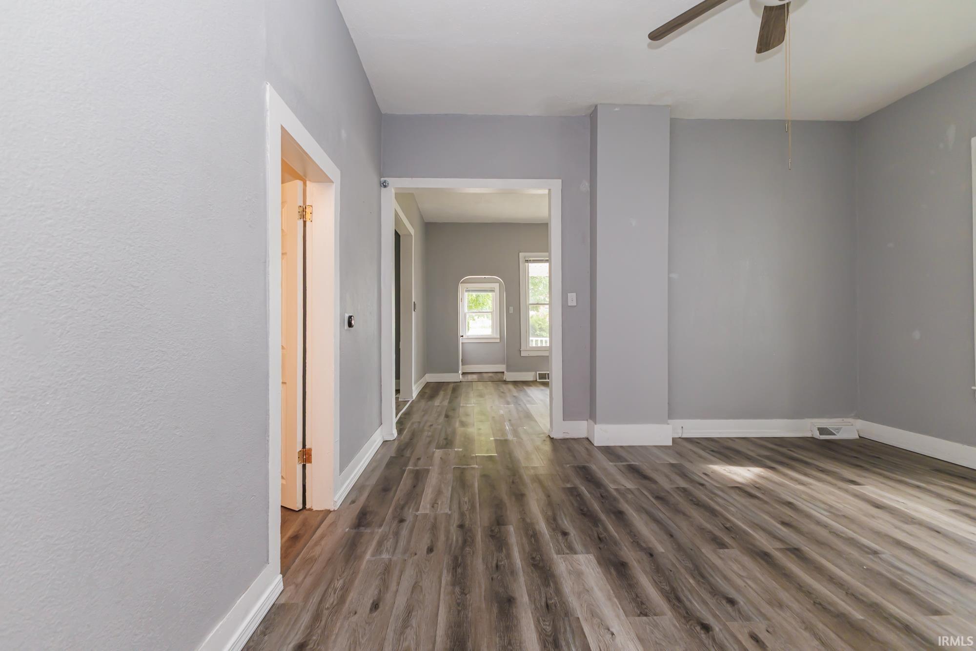 Spacious room featuring wood-finish flooring, light grey painted walls, white trim, and an overhead ceiling fan