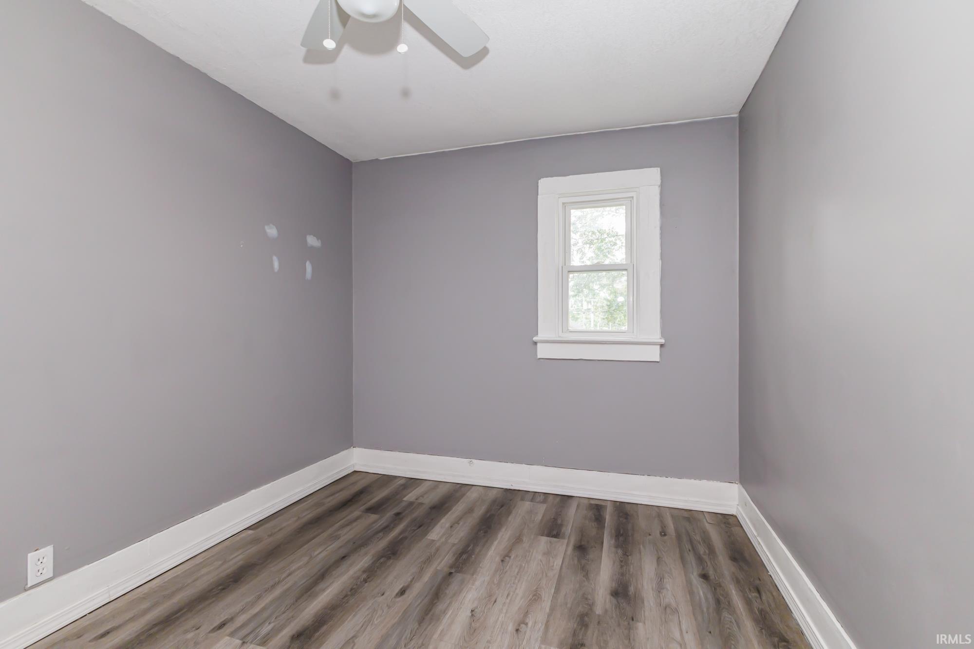 Room with neutral gray walls, wood-finish flooring, white trim, and a white ceiling fan
