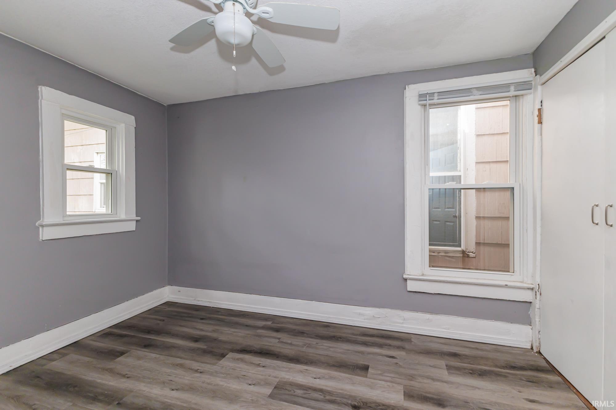 Room featuring light gray walls, wood-finish flooring, white trim, and a ceiling fan