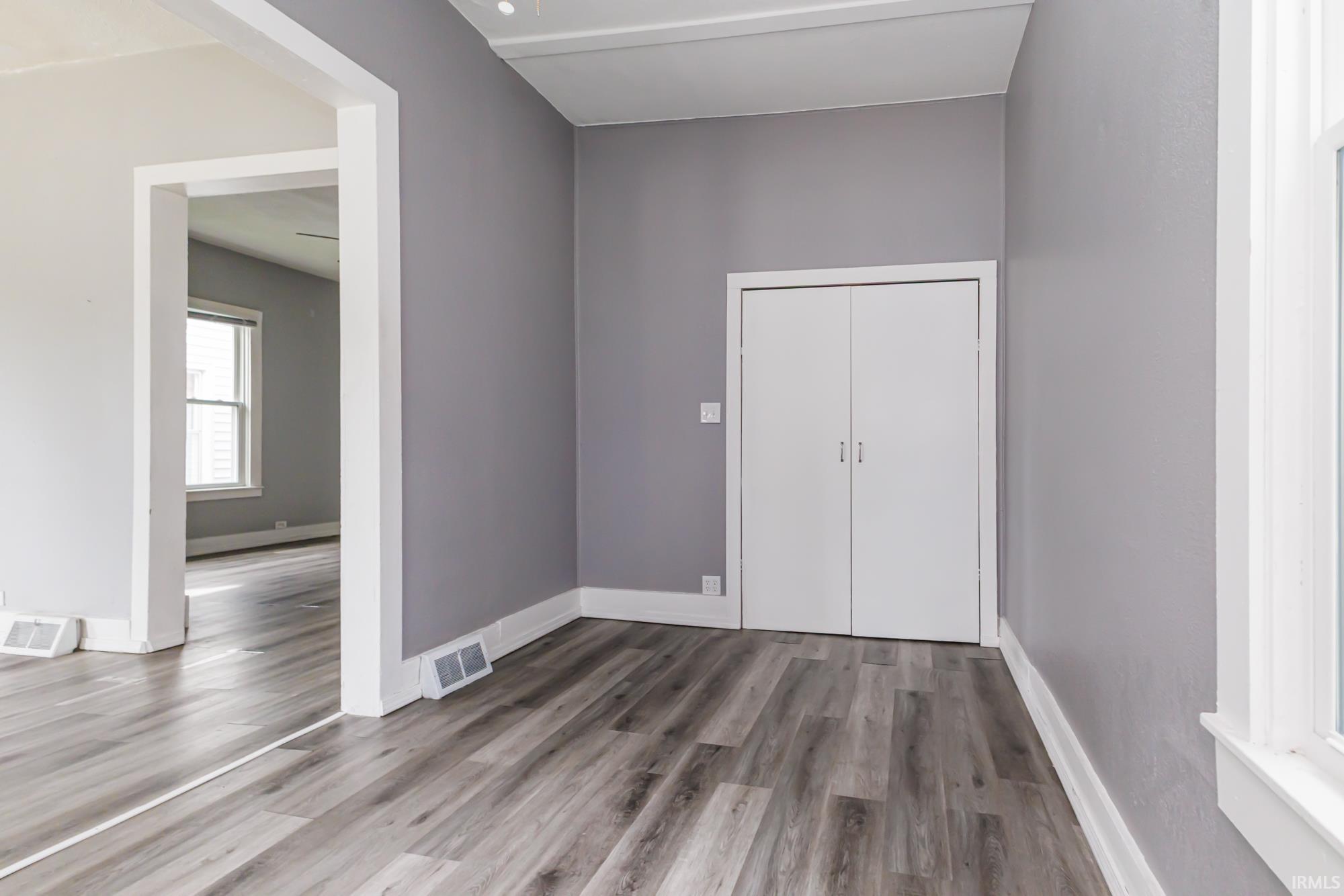 Spacious interior featuring wood-finish flooring, light gray walls, white trim, and a bi-fold closet