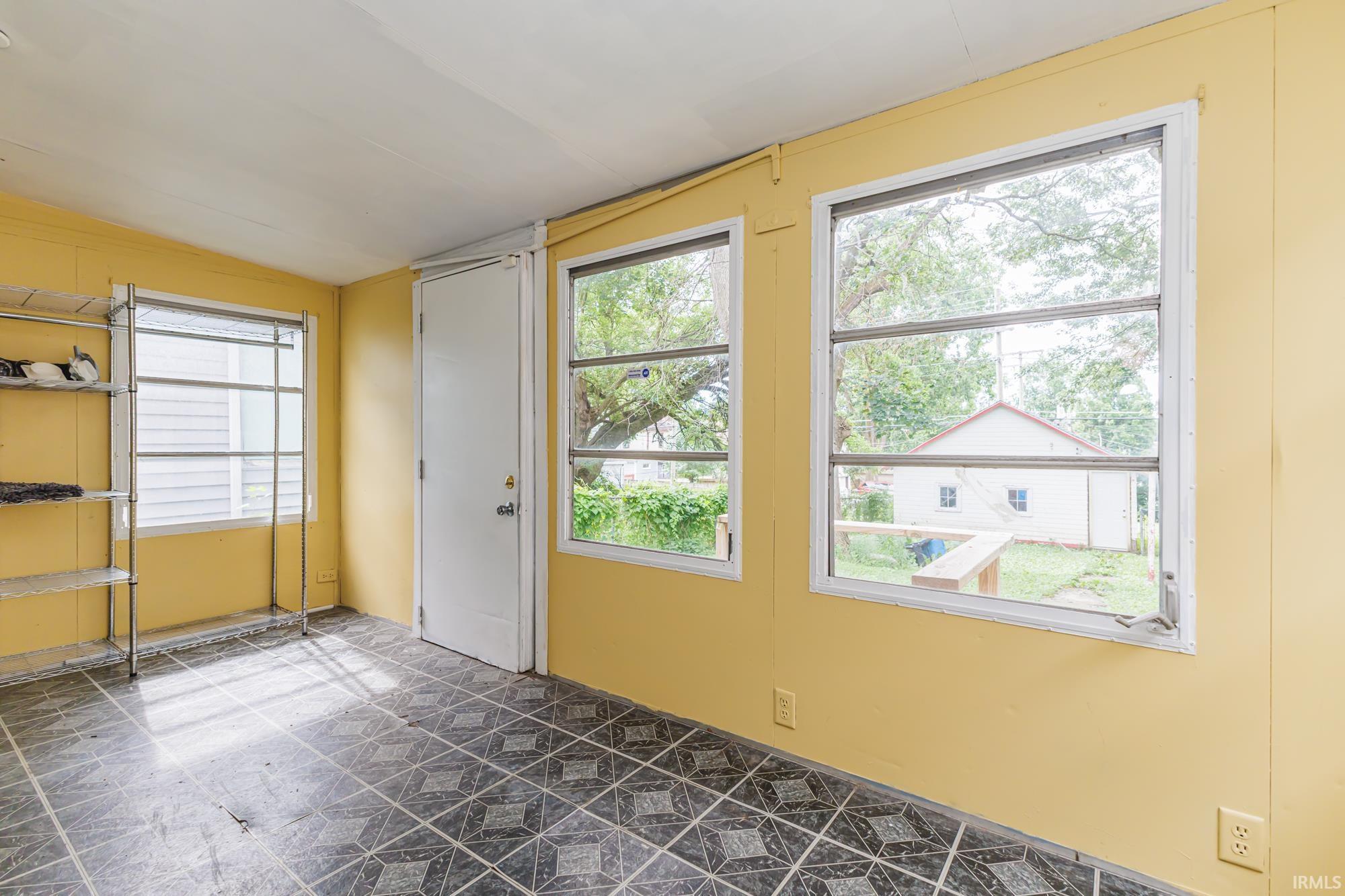 Room featuring patterned tile flooring, multiple windows, a solid white door, and yellow walls