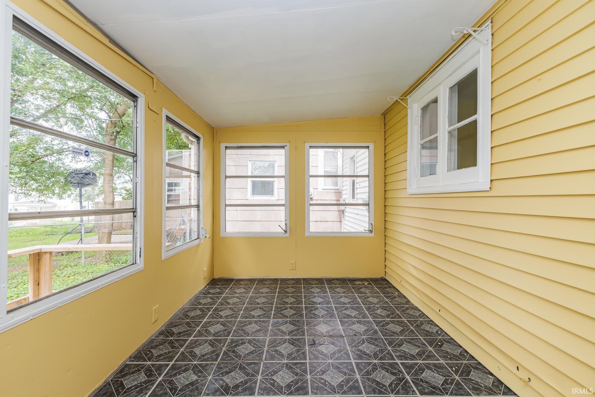 Enclosed porch featuring multiple windows, vinyl siding, a painted ceiling, and patterned tile flooring