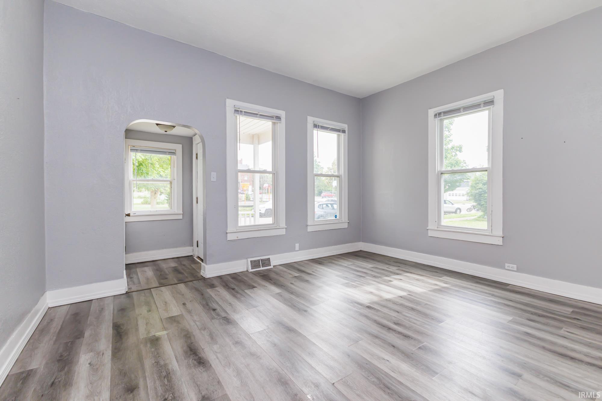 Spacious room featuring light gray walls, white trim, wood-finish flooring, and multiple windows