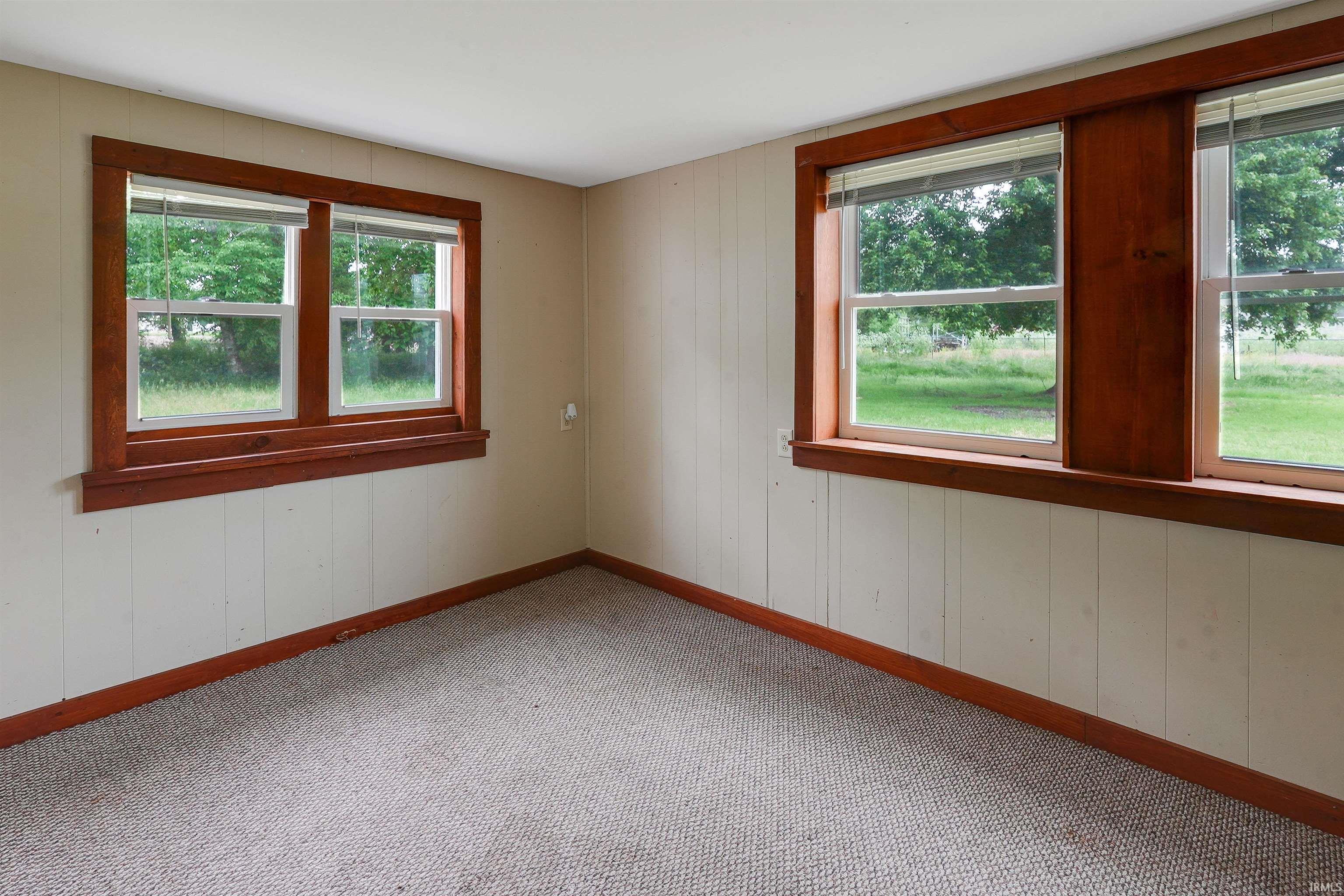 Carpeted room featuring two window sets with wood-trim framing, vertical paneling on lower walls, and a muted wall color