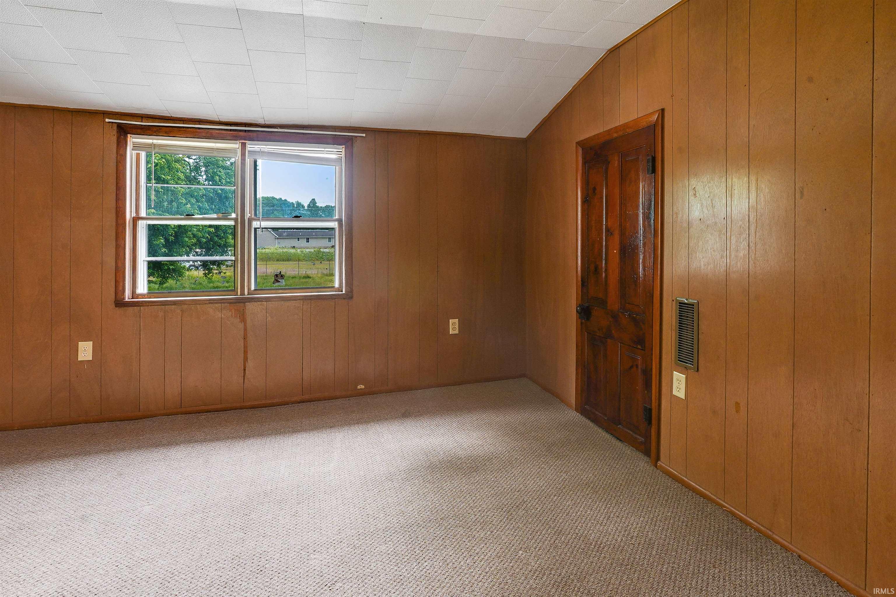 Carpeted room featuring wood-paneled walls, a wood-frame window, and a wooden paneled door