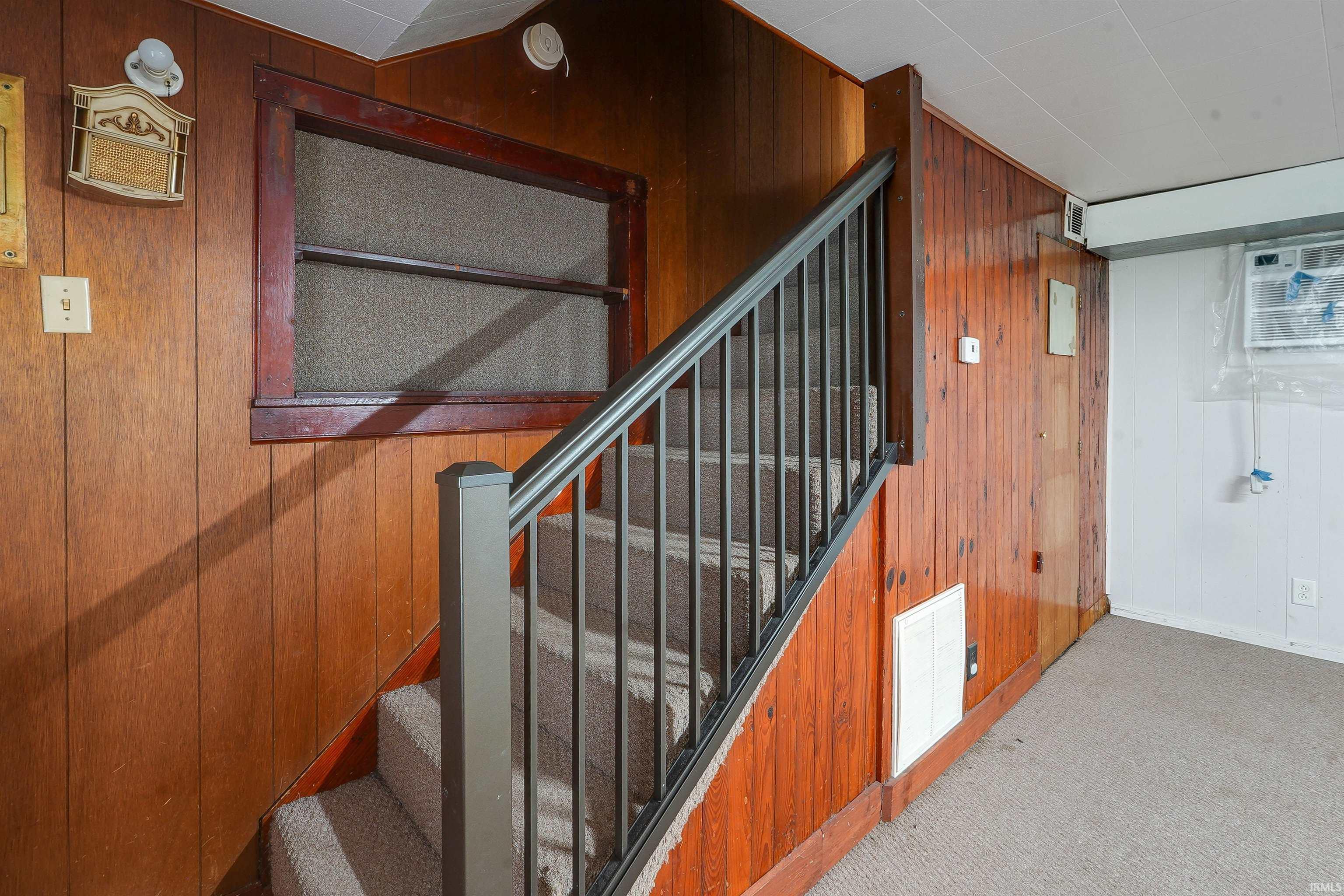 Carpeted staircase with dark metal balusters and wood newel post, framed by vertical wood paneling