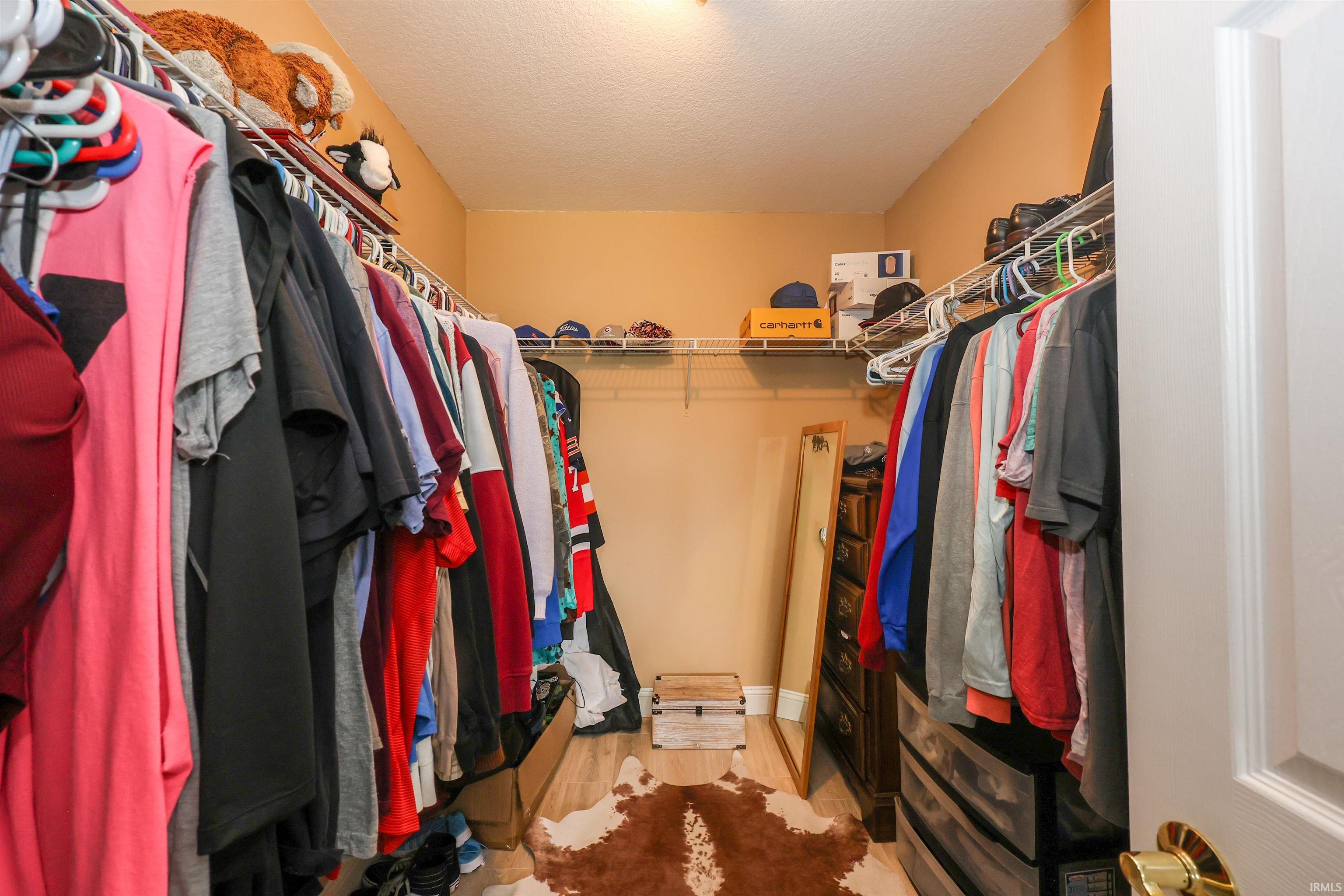 Walk-in closet with overhead lighting, wire shelving, and wood-finish flooring