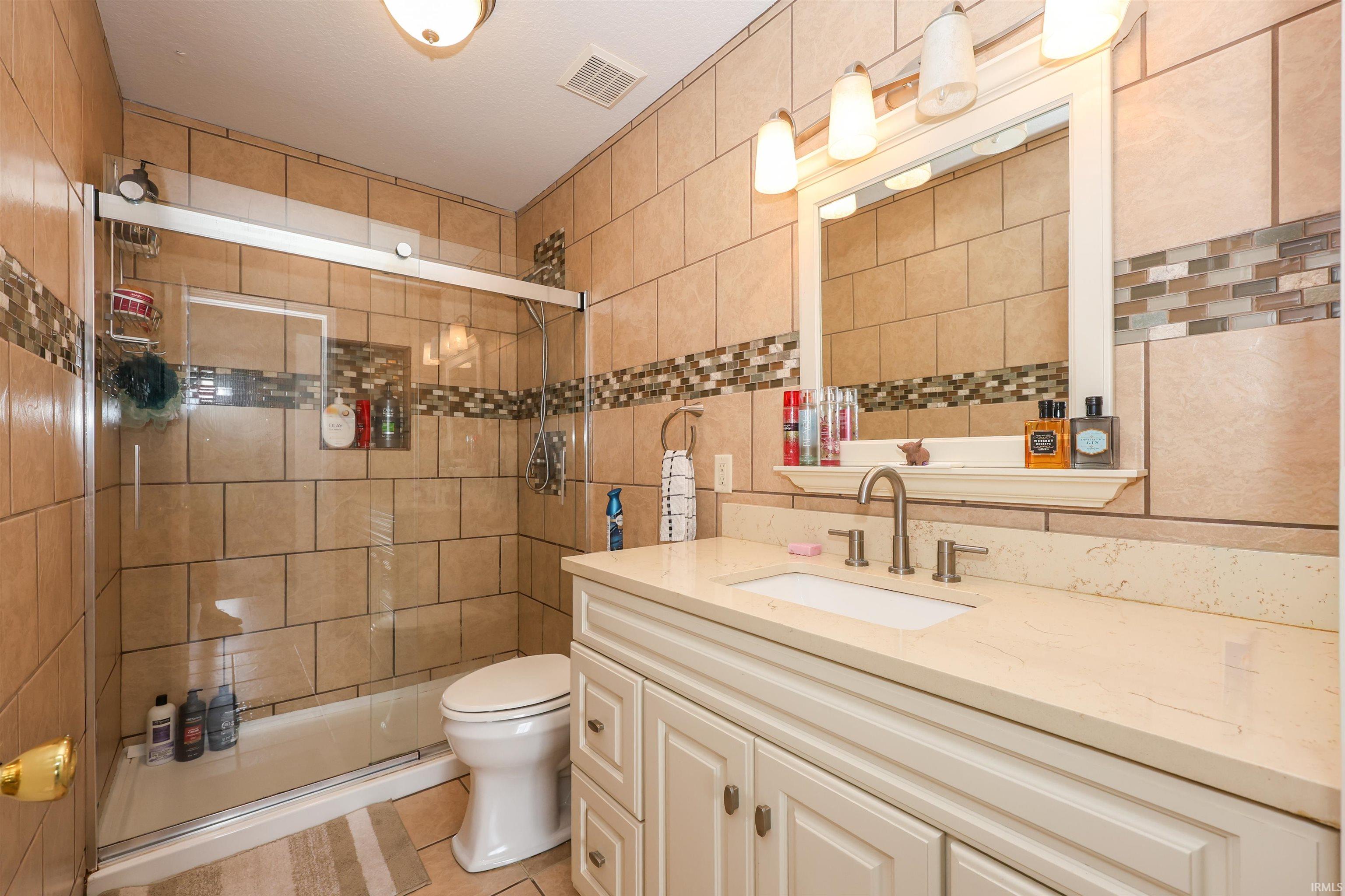Bathroom featuring a glass-enclosed shower with tile surround, a single vanity with a light-colored countertop, and a framed mirror with overhead lighting