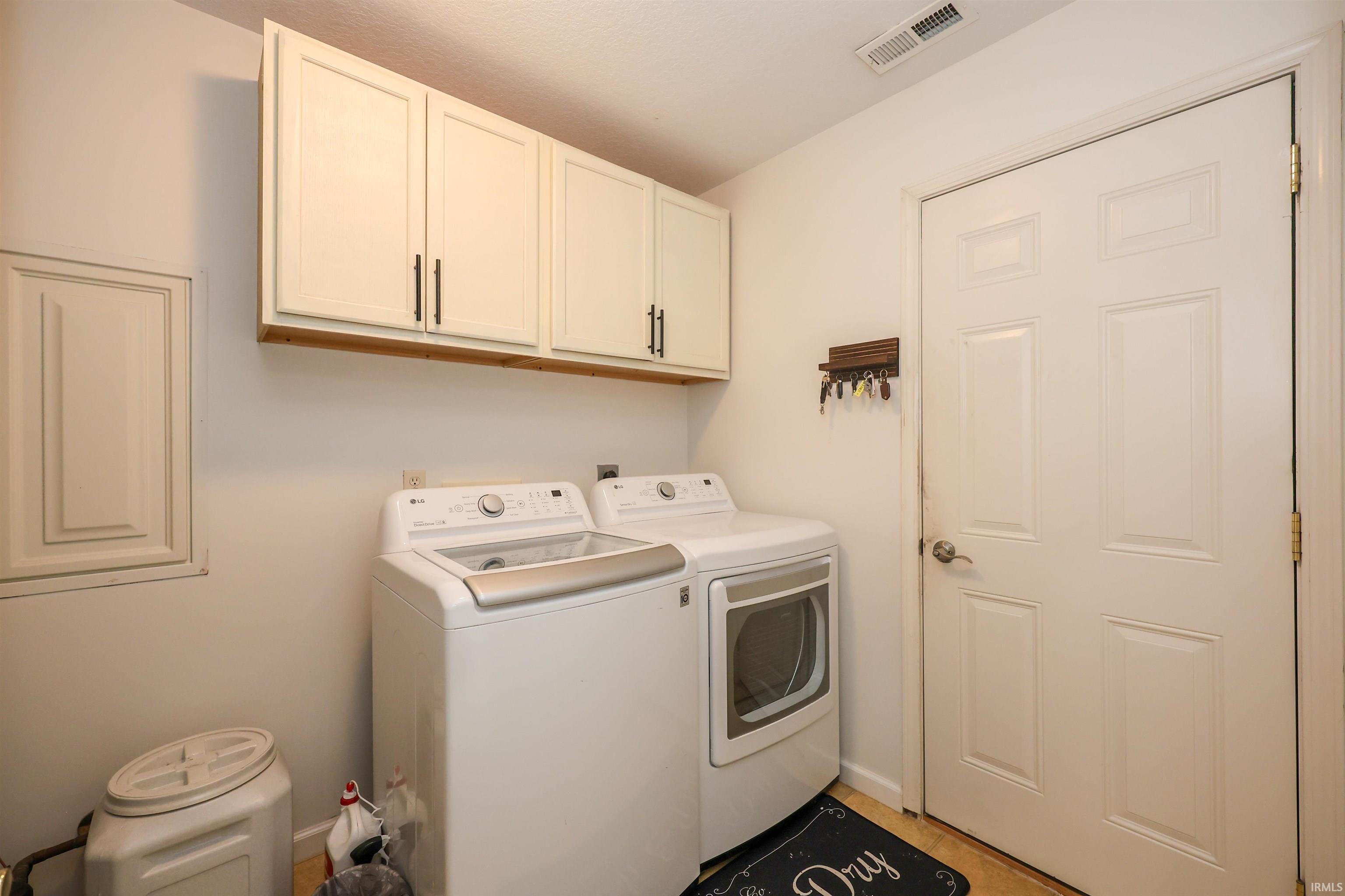 Laundry area featuring white cabinetry with dark hardware, a white six-panel door, and tiled flooring