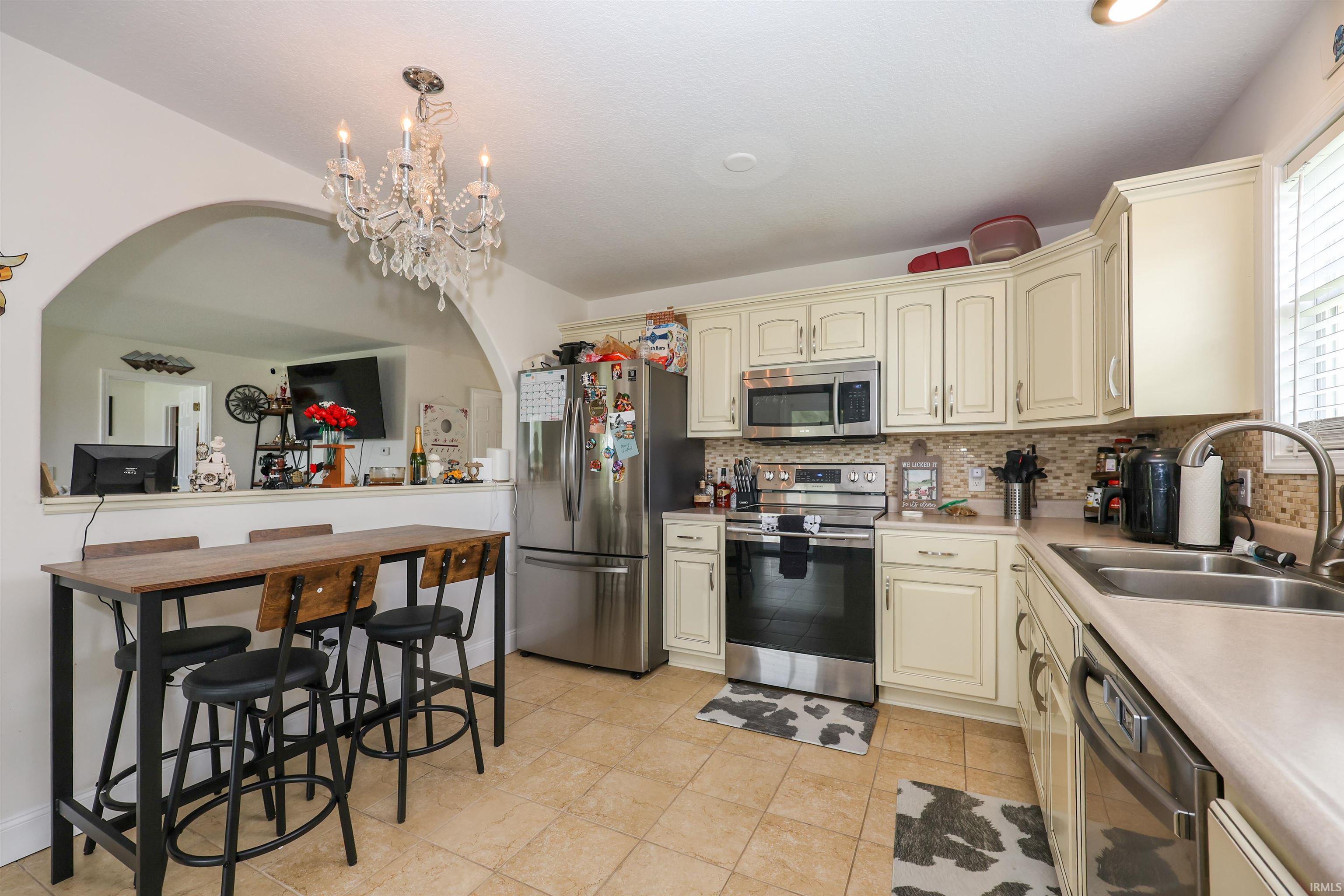 Kitchen featuring tile flooring, cream-colored cabinetry, stainless steel appliances, and a mosaic tile backsplash