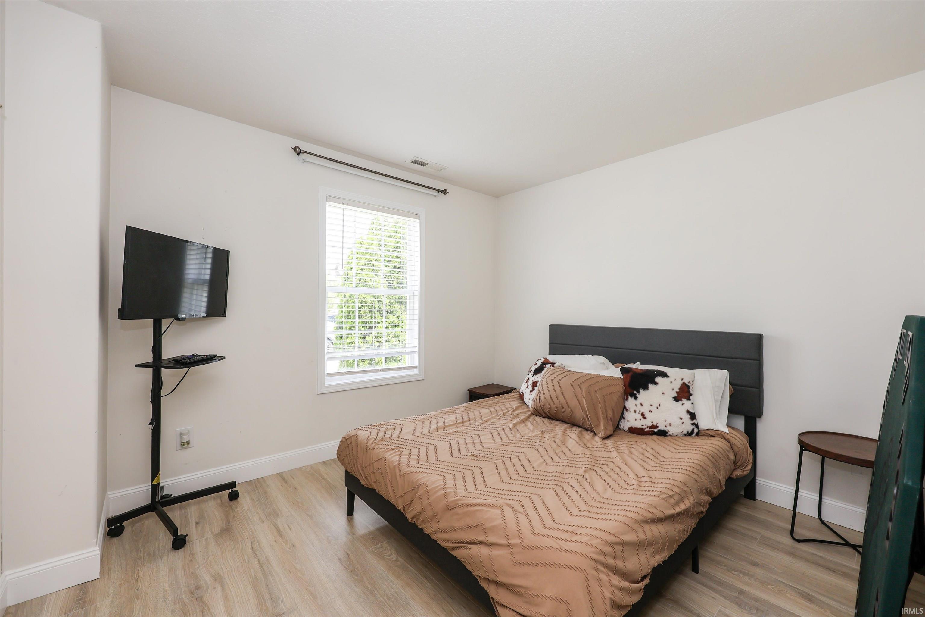 Bright room featuring light wood-finish flooring, white walls, and a window with blinds