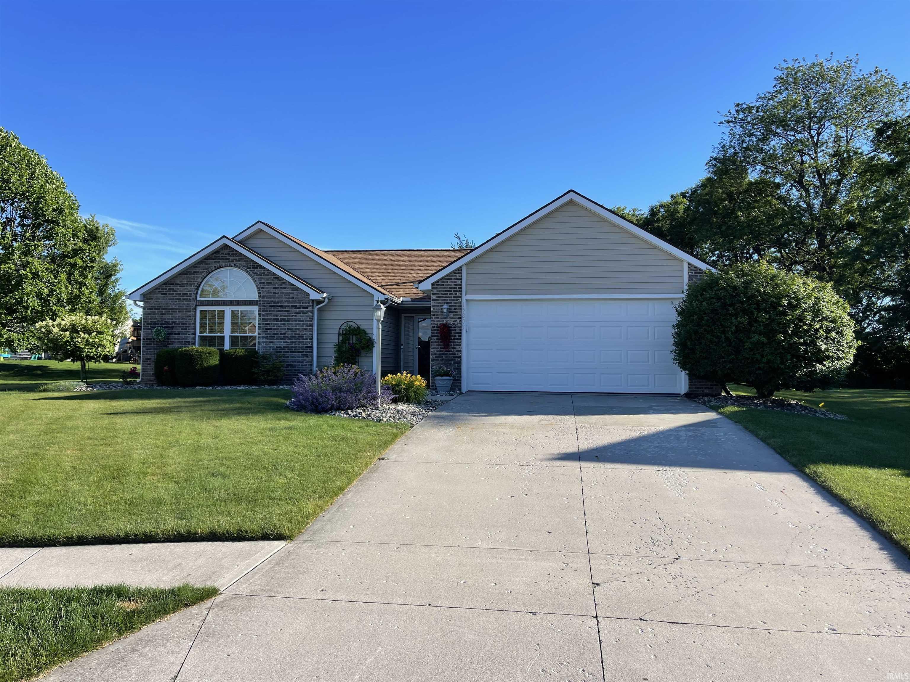 Exterior featuring a stone and siding facade, arched window, attached garage, concrete driveway, and established landscaping