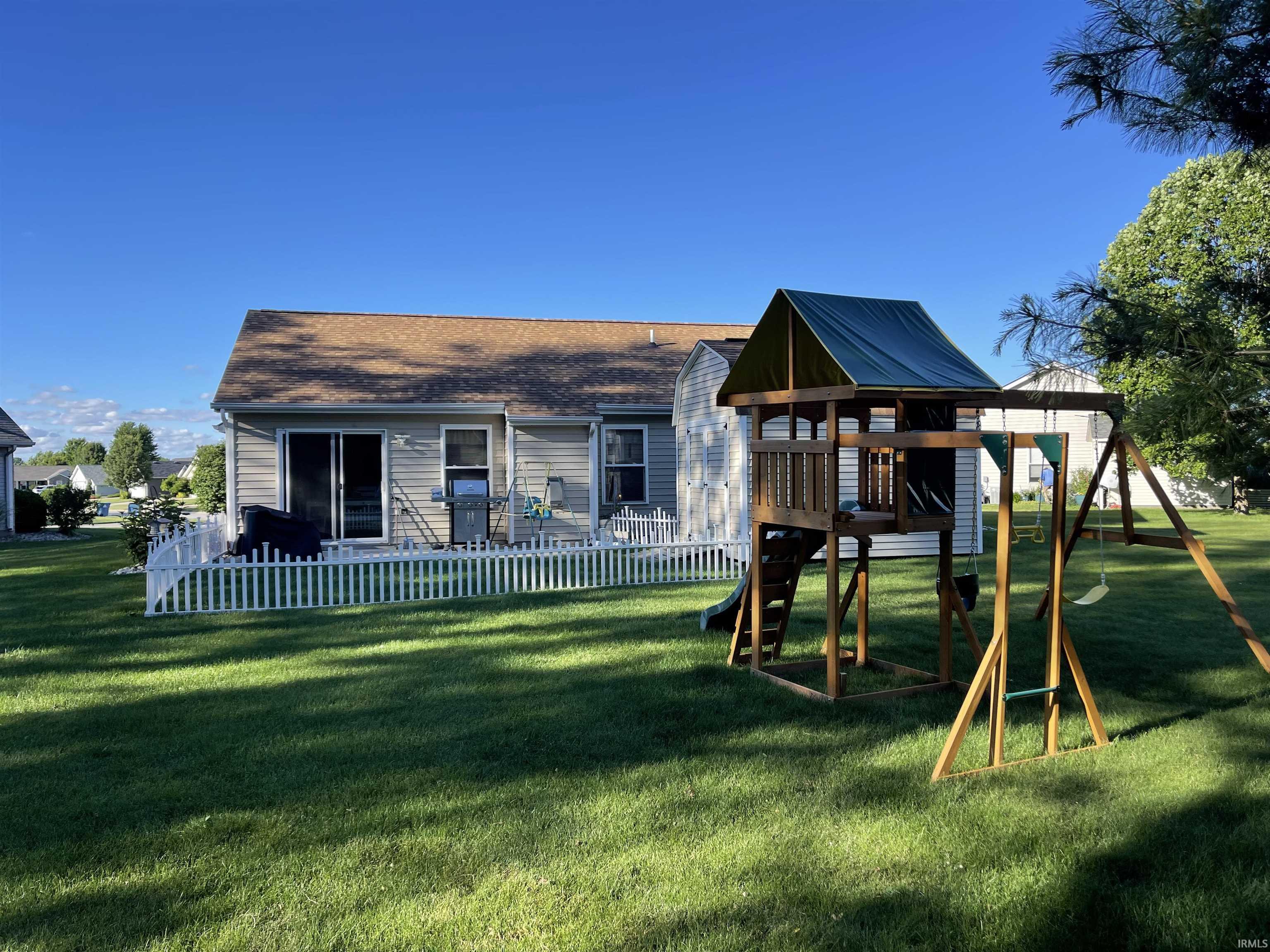 Expansive rear yard featuring a manicured lawn, a white picket fence, and a wooden playset with a green canopy