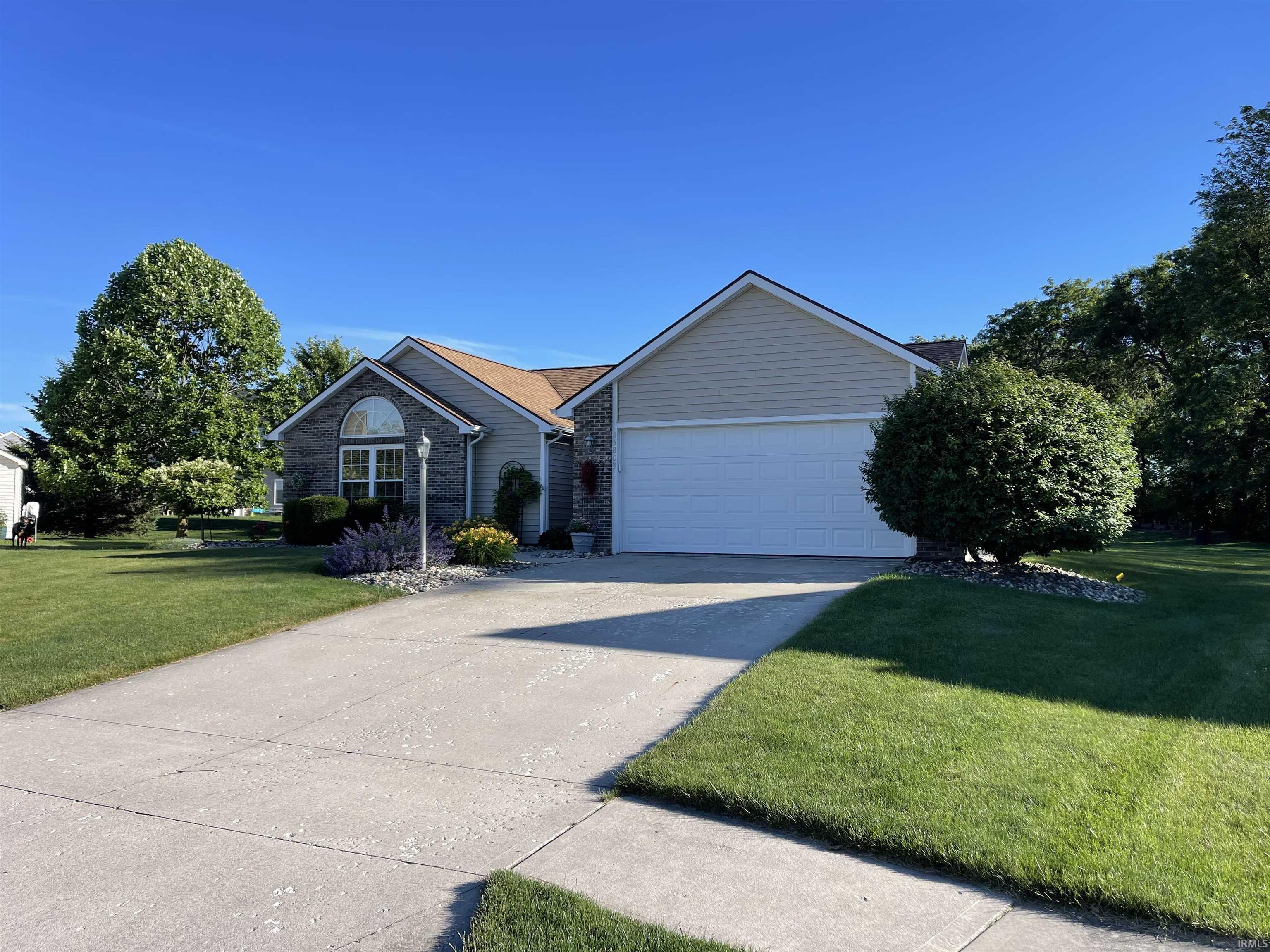 Single-story residence featuring a two-car garage, stone and siding exterior, arched window with grid detailing, concrete driveway, and mature landscaping