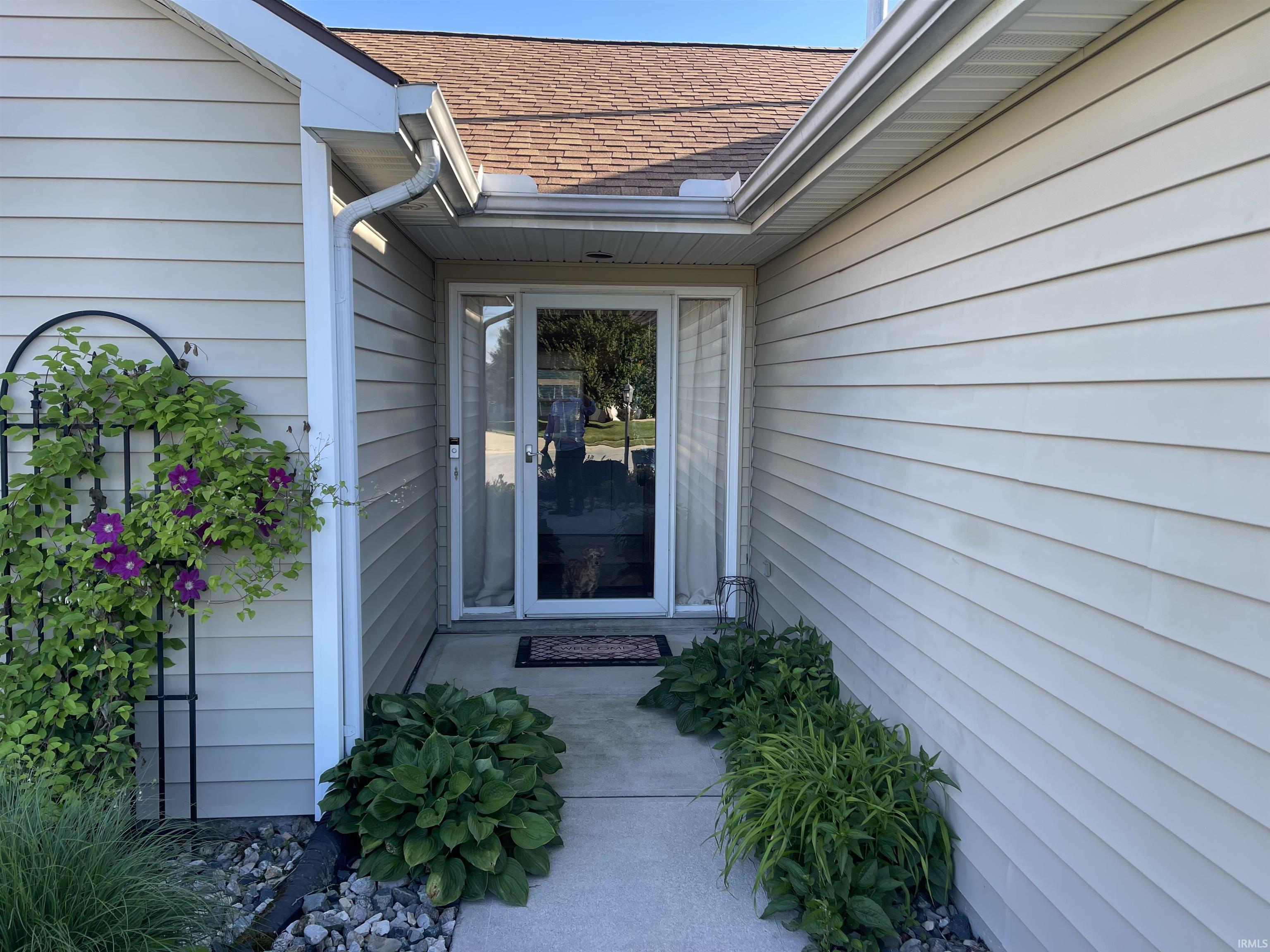 Inviting entry featuring a storm door, concrete walkway, and a landscaped bed with hostas and decorative rocks