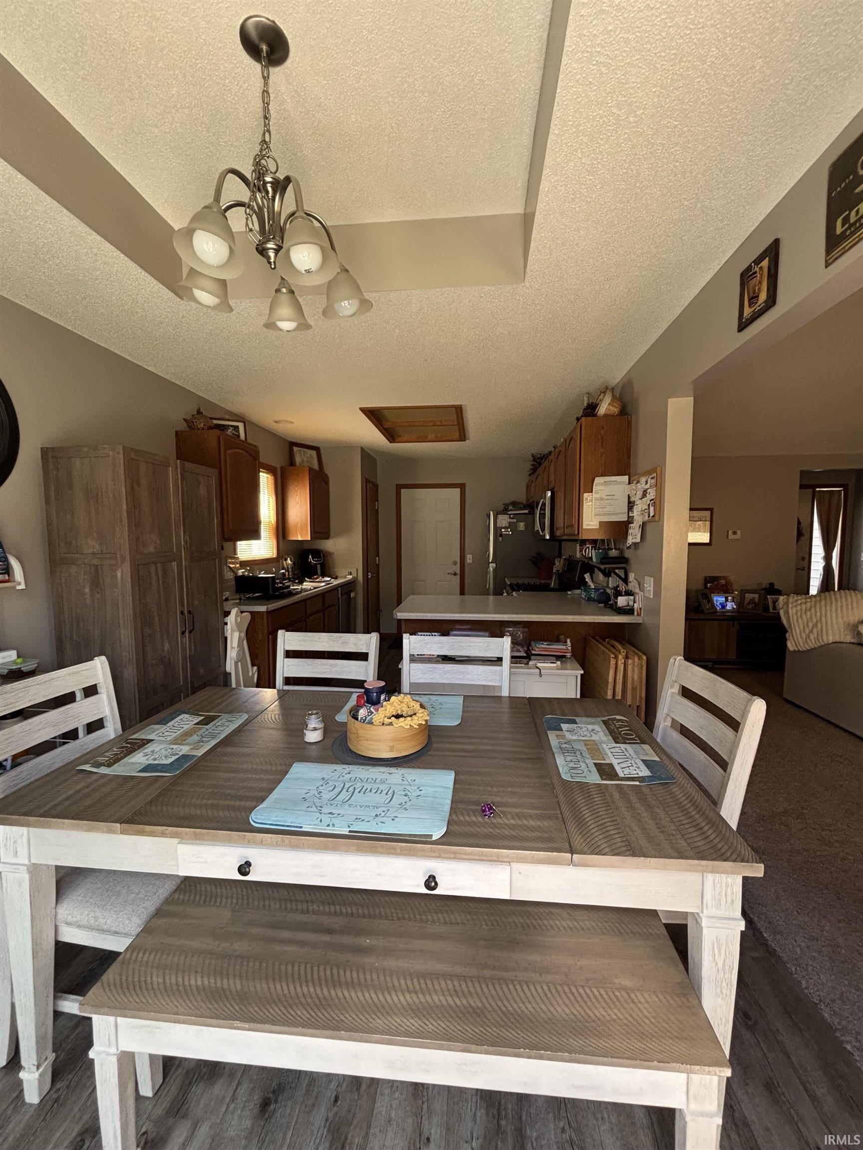 Dining area featuring a tray ceiling with a five-light chandelier, wood-finish flooring, and a dining table with a contrasting wood-finish top and white-painted base