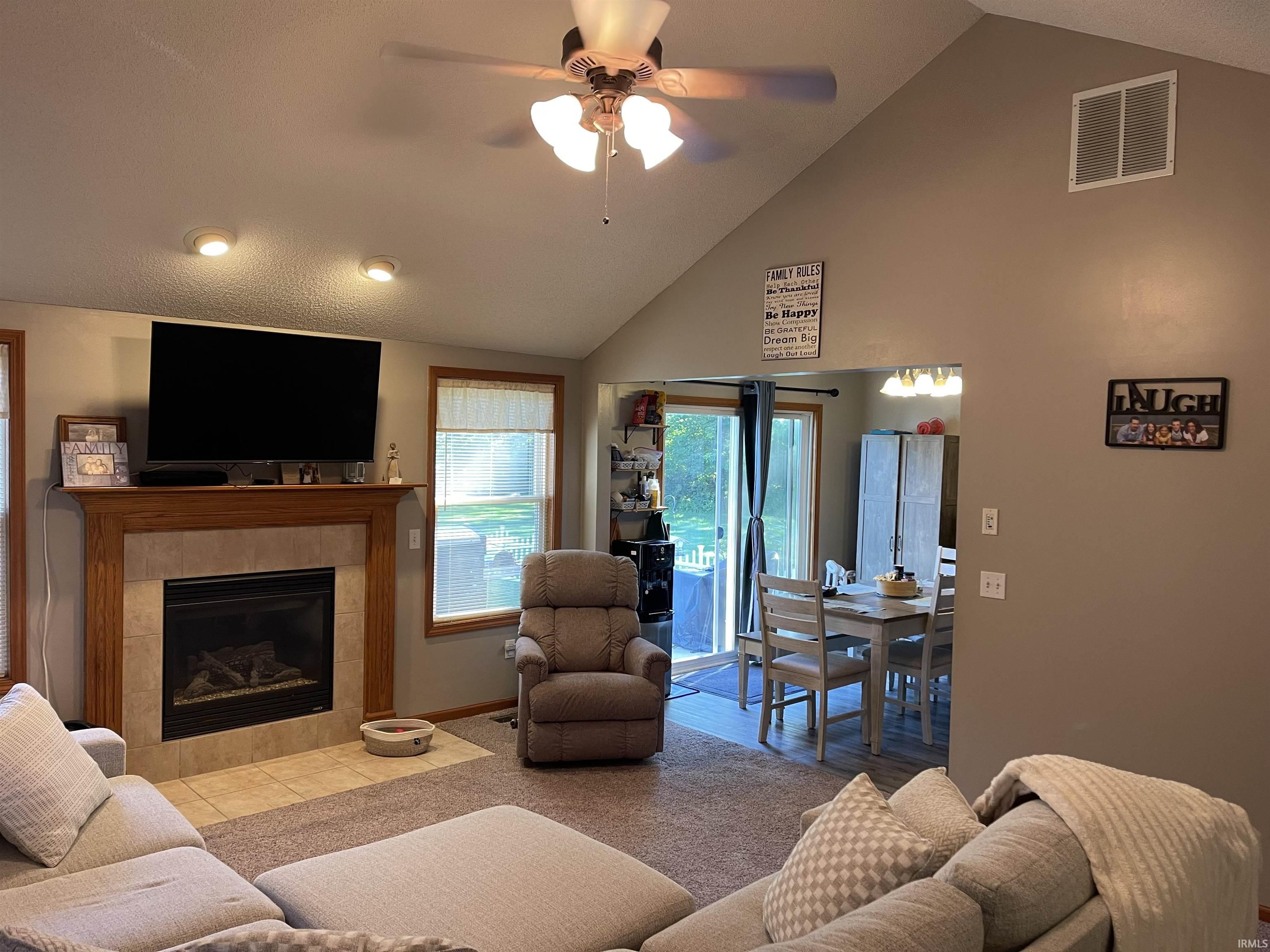 Living area featuring vaulted ceilings with a ceiling fan, recessed lighting, and a fireplace with a wood mantle and tile surround
