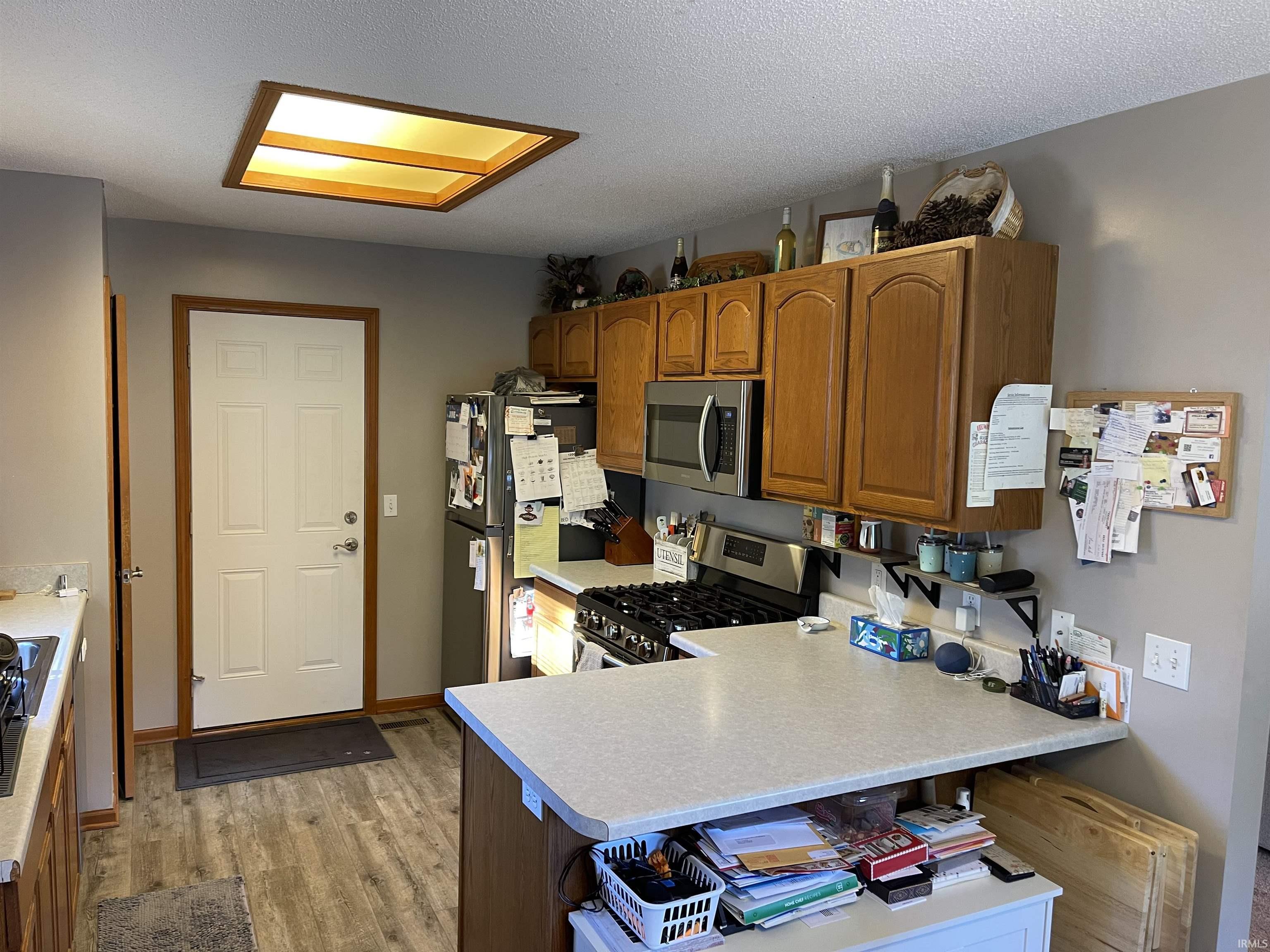 Kitchen featuring wood-finish flooring, a contemporary ceiling light fixture, wood cabinetry, a stainless steel microwave, and a gas range