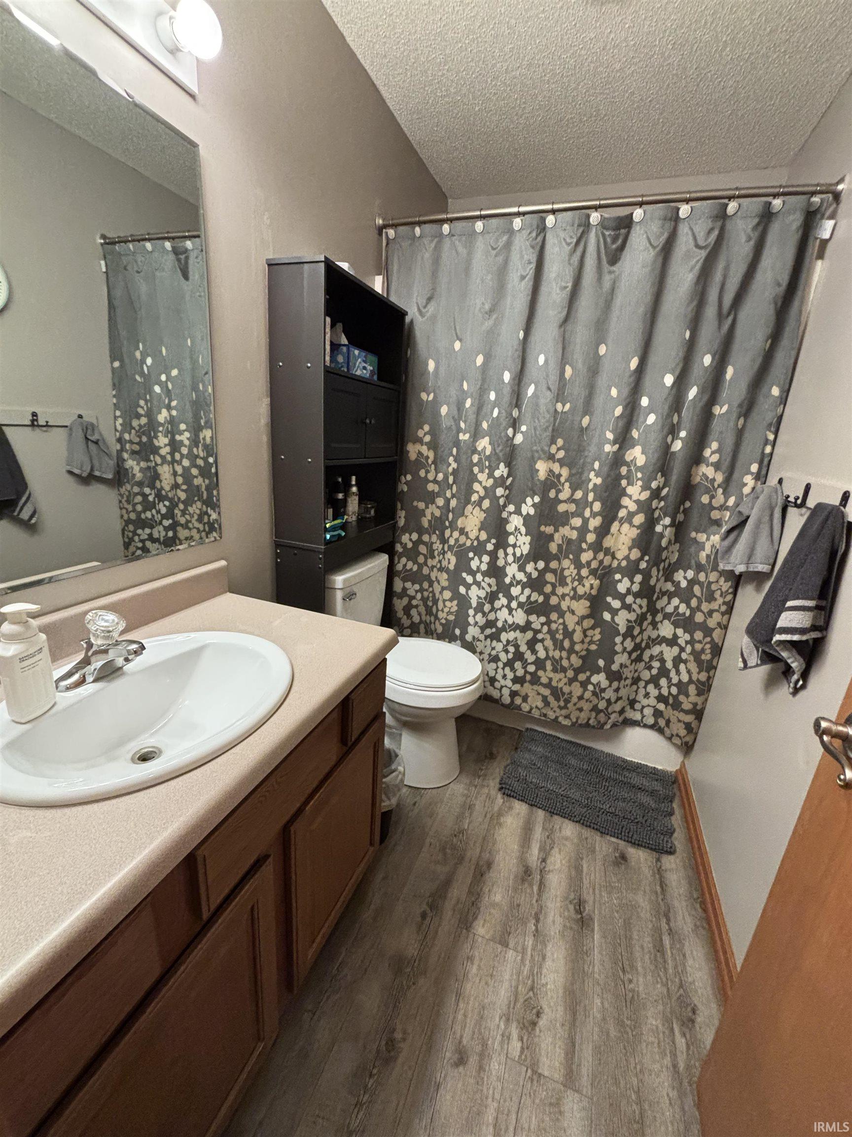 Bathroom featuring wood-finish flooring, a white porcelain toilet, a vanity with wood cabinetry, a beige countertop, and an oval sink