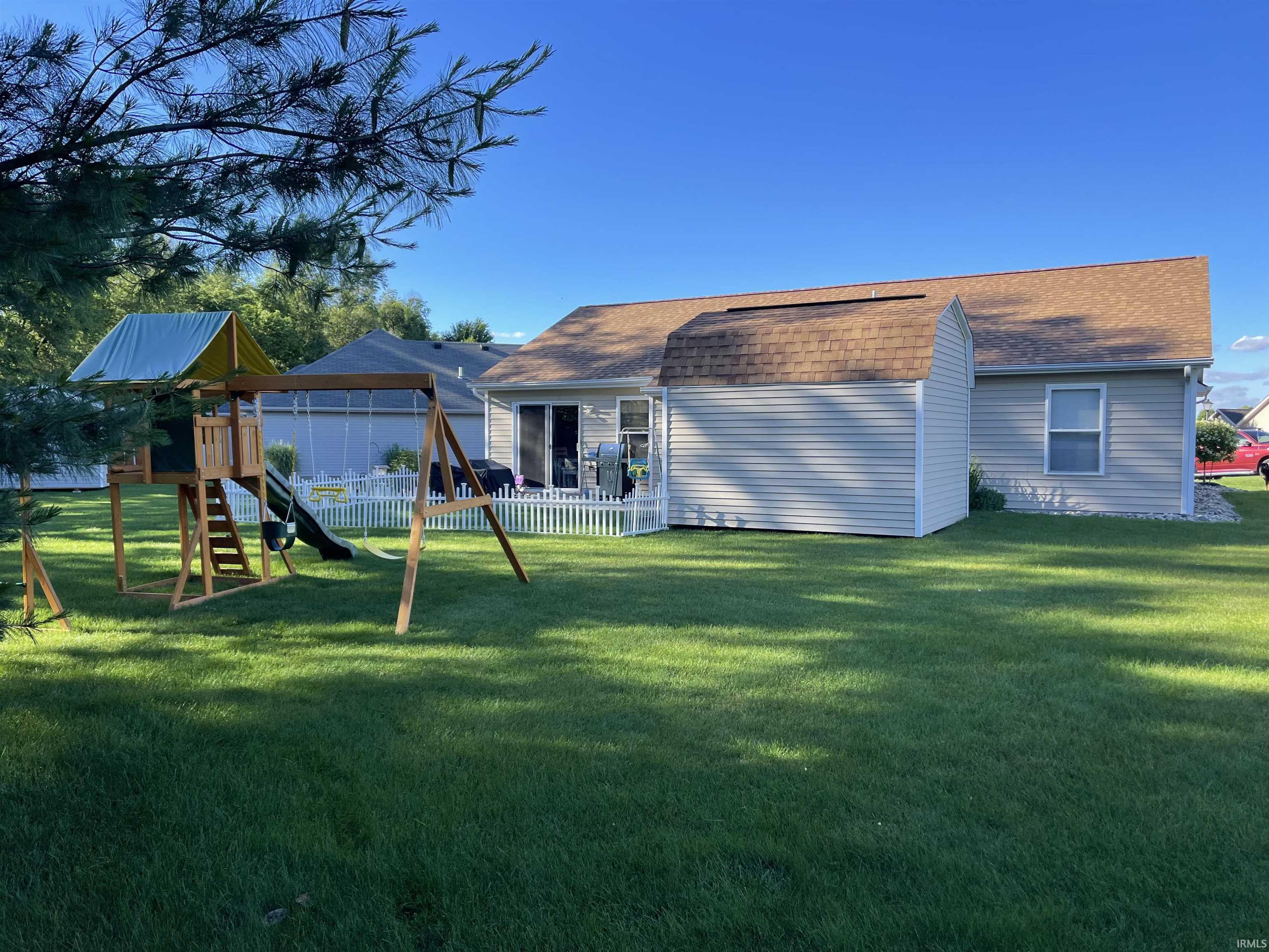 Expansive backyard featuring a lush lawn, white picket fencing, and a patio with sliding glass doors