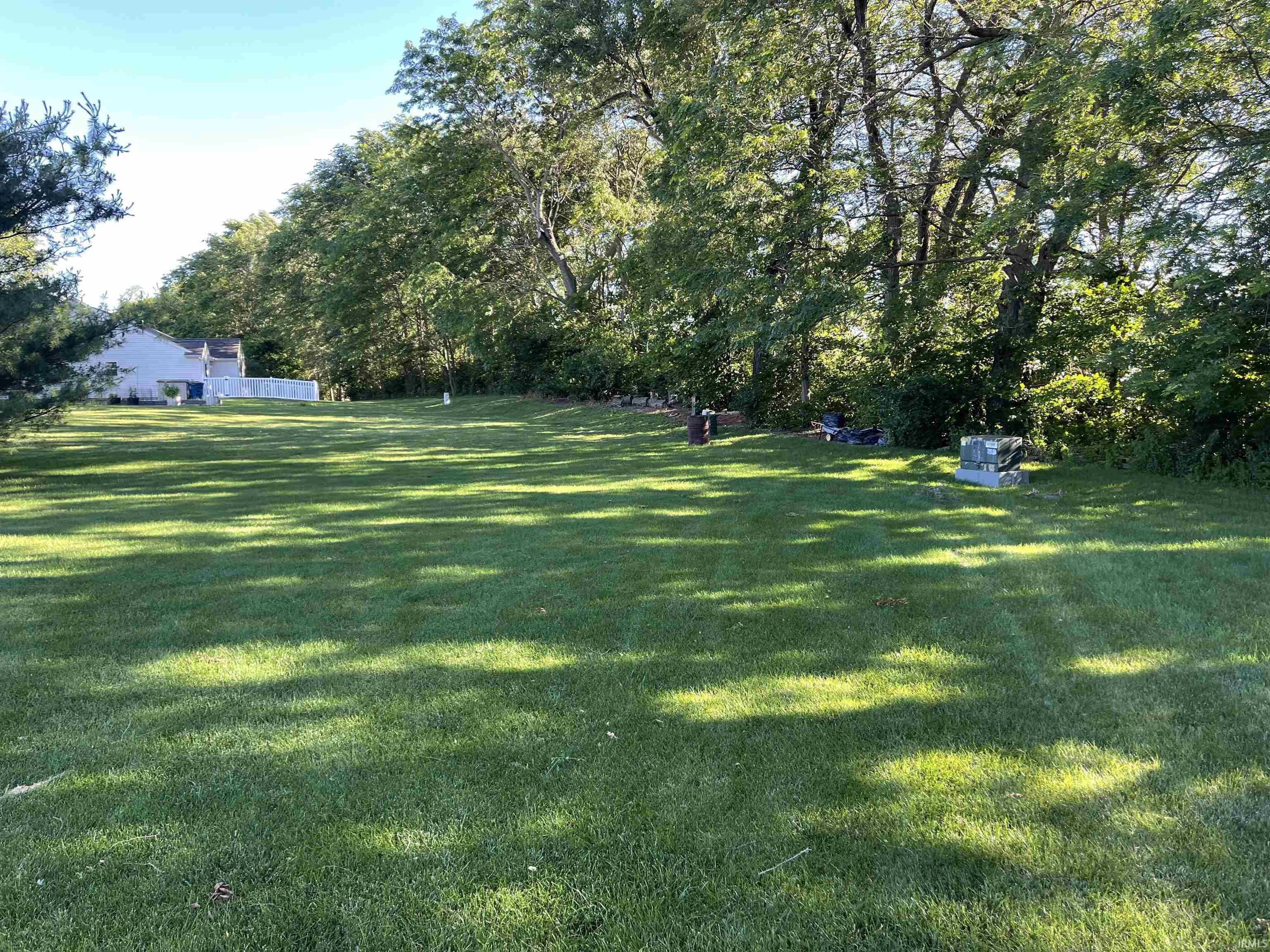Expansive lawn area with mature trees and a partial white privacy fence