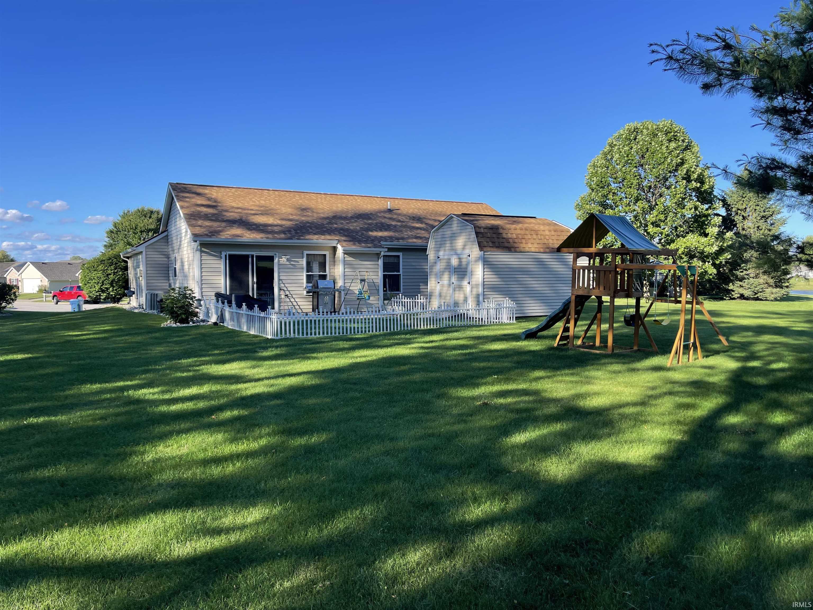 Expansive rear yard featuring a large green lawn, a white fenced deck, sliding glass door access, and mature perimeter trees