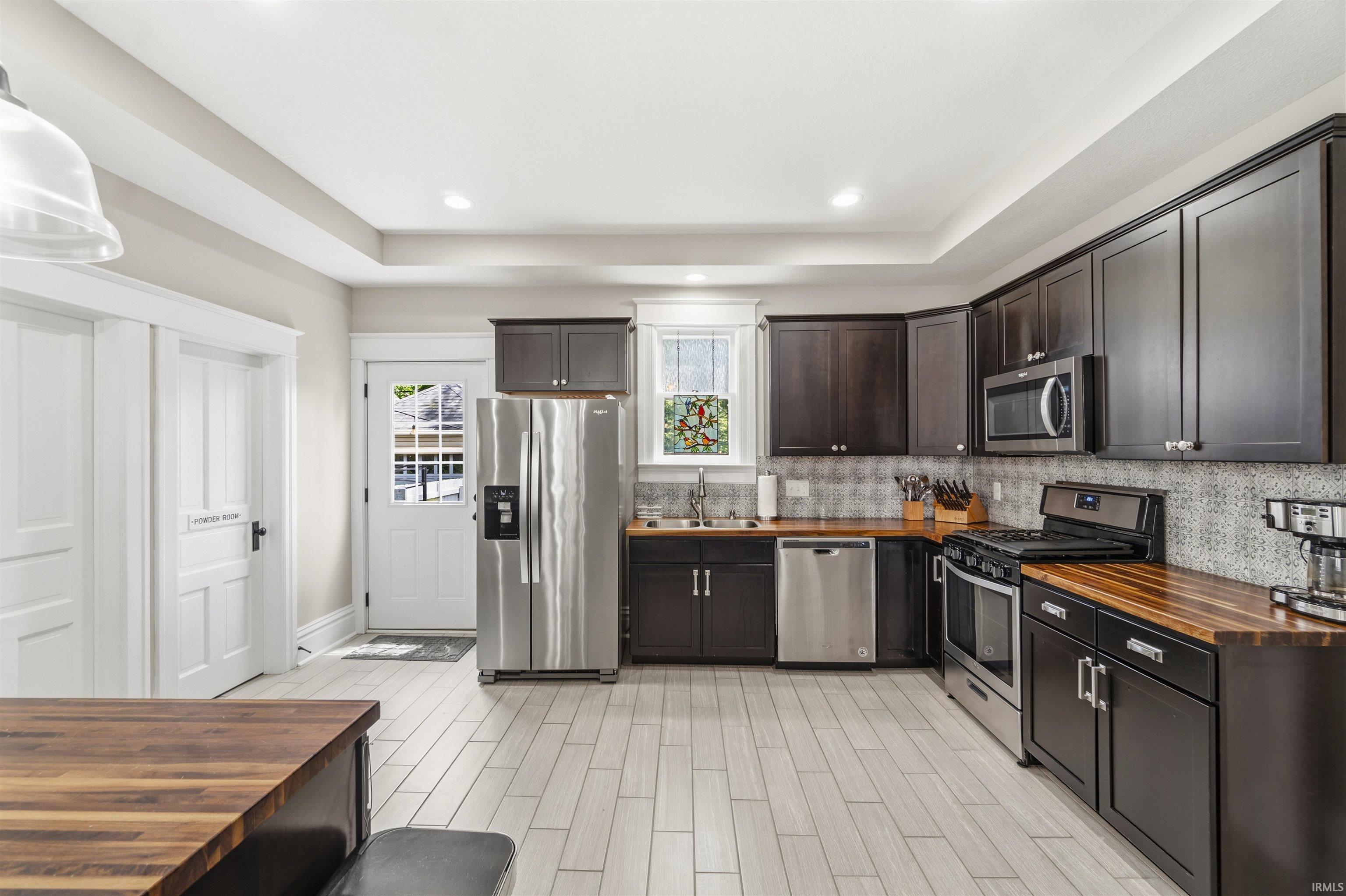 Kitchen featuring dark wood cabinetry, stainless steel appliances, wood-finish countertops, and light-toned plank flooring