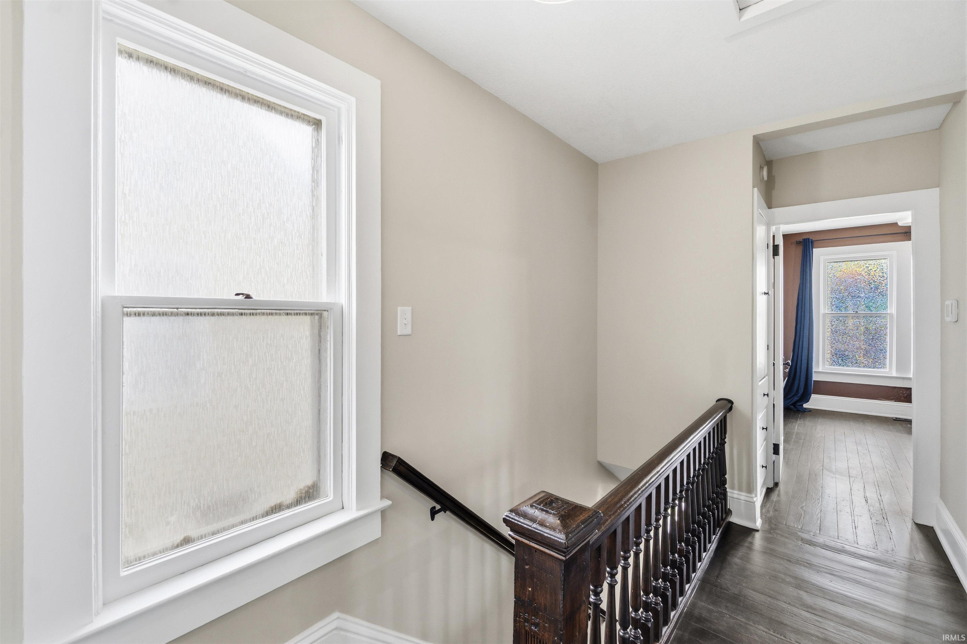 Upper landing featuring dark wood-finish flooring, a white-framed window with textured glass, and a dark wood banister with ornate spindles
