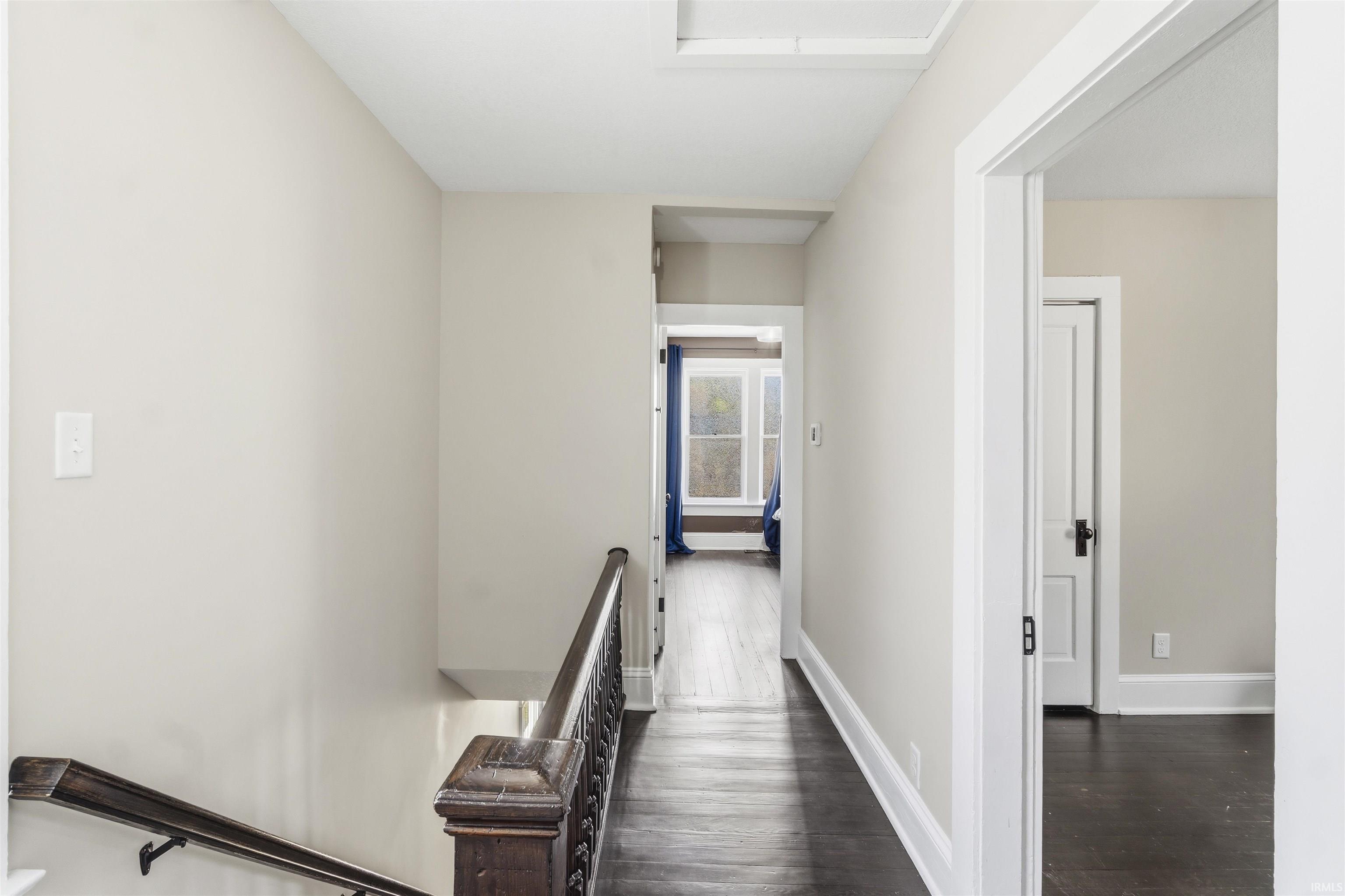 Hallway featuring rich wood-finish flooring, light neutral wall paint, and white trim