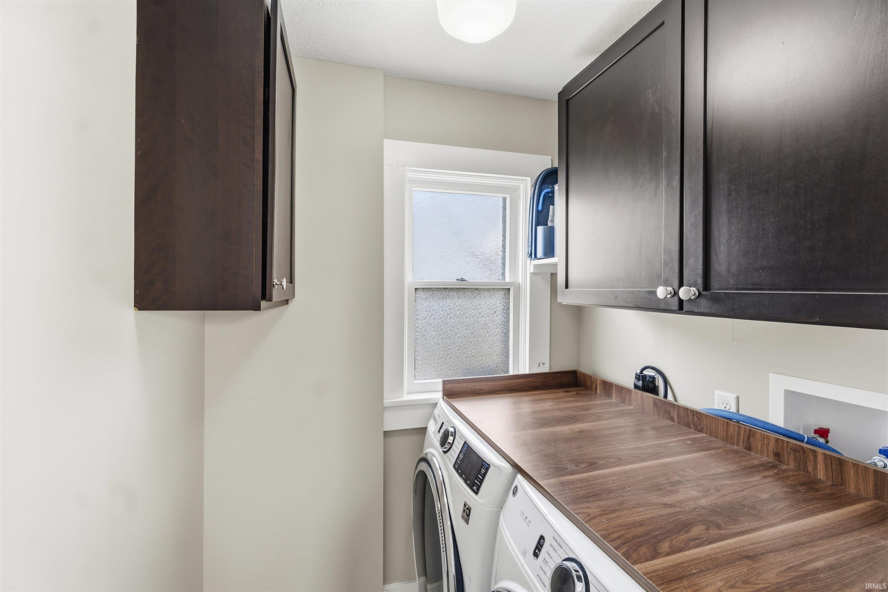 Laundry area featuring a wood-finish countertop, dark cabinetry, and white appliances