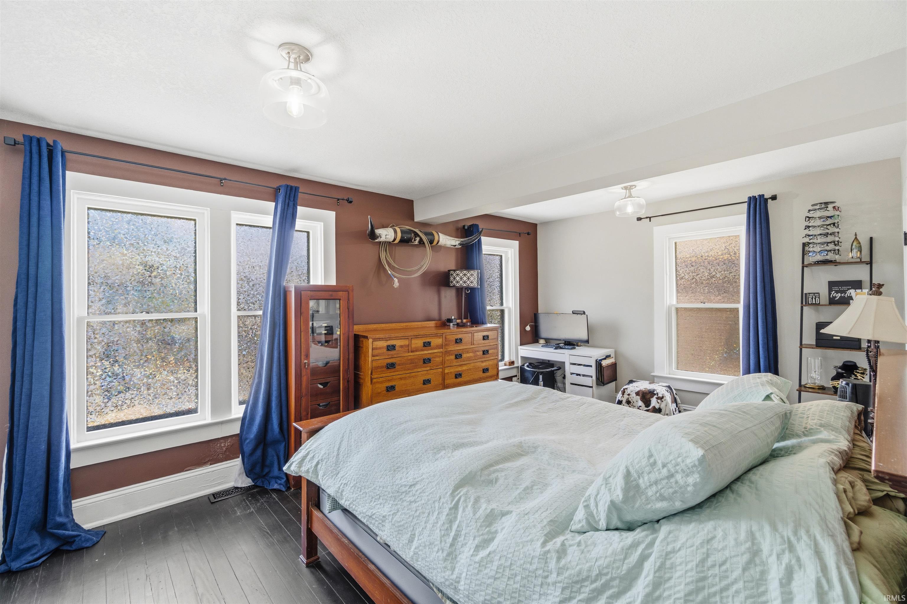 Spacious room featuring dark wood-finish flooring, multiple windows with privacy glass, recessed ceiling beams, and contemporary flush-mount lighting fixtures
