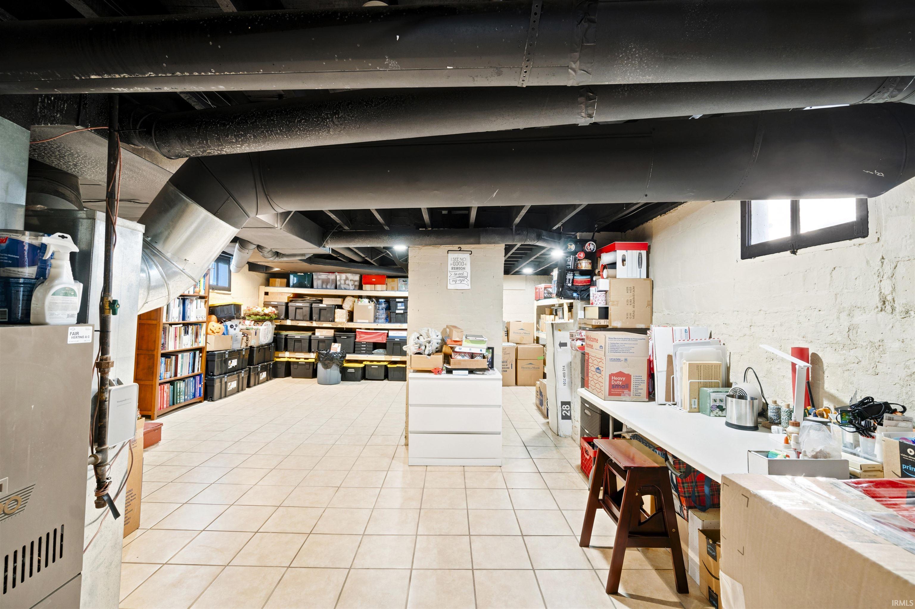 Spacious basement area featuring tile flooring, exposed ceiling beams, and painted concrete block walls