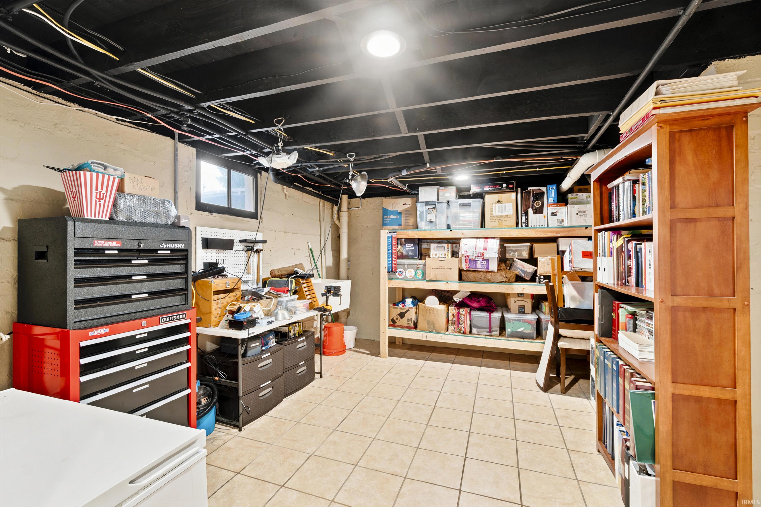 Finished basement space featuring light-toned tile flooring, exposed black ceiling joists, and a perimeter window