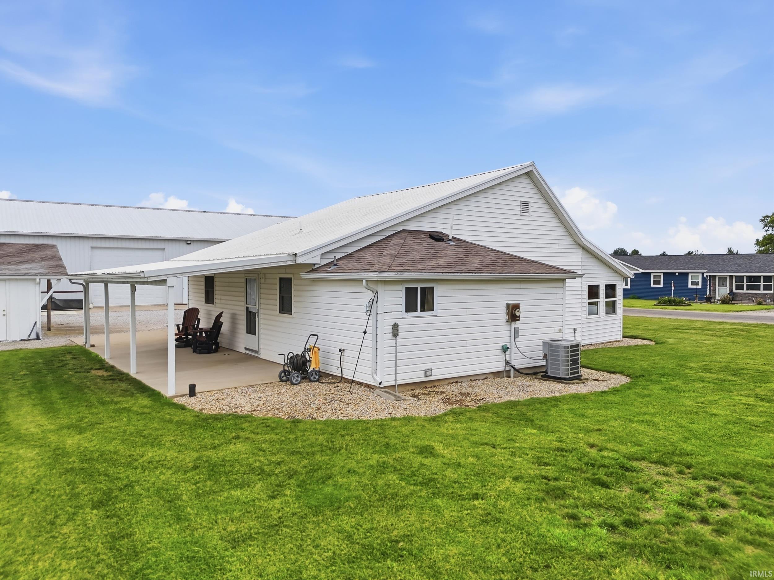 White siding exterior featuring a covered concrete patio, a gravel border, and a green lawn