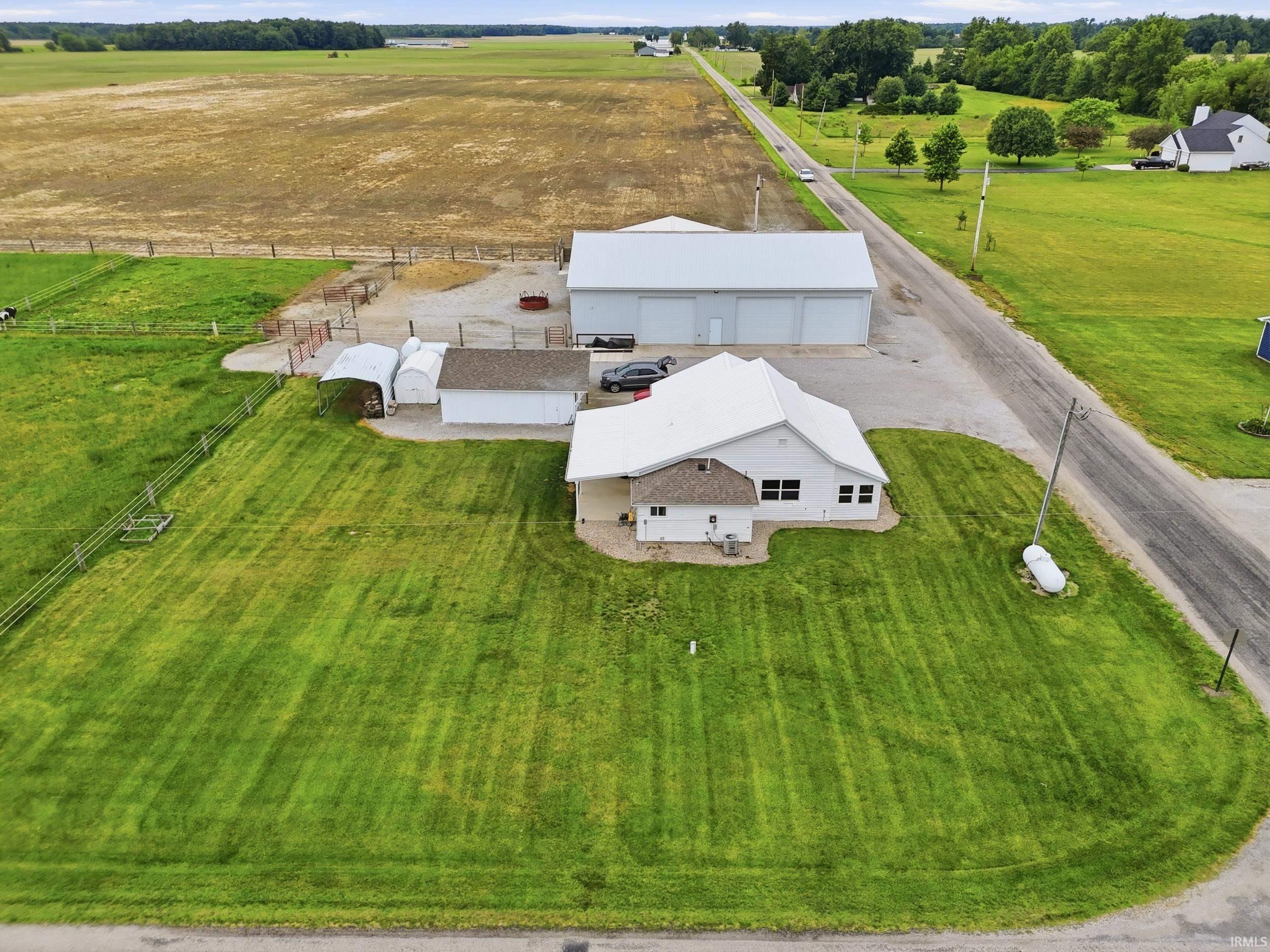 Expansive property featuring a white residence with a metal roof, a large outbuilding with multiple bay doors, additional smaller outbuildings, and extensive green space