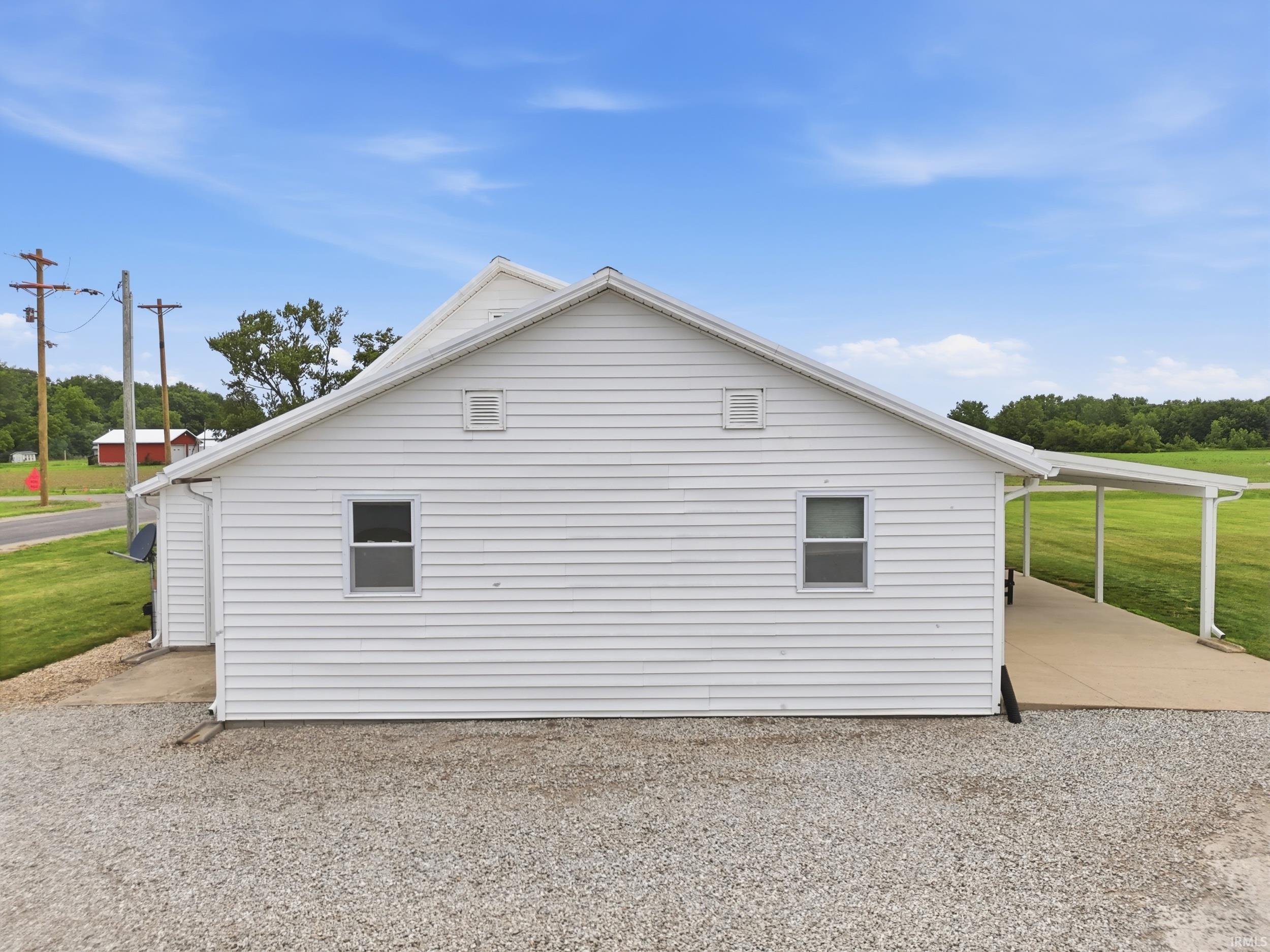 White siding exterior featuring two windows, a gabled roofline, and a covered concrete patio