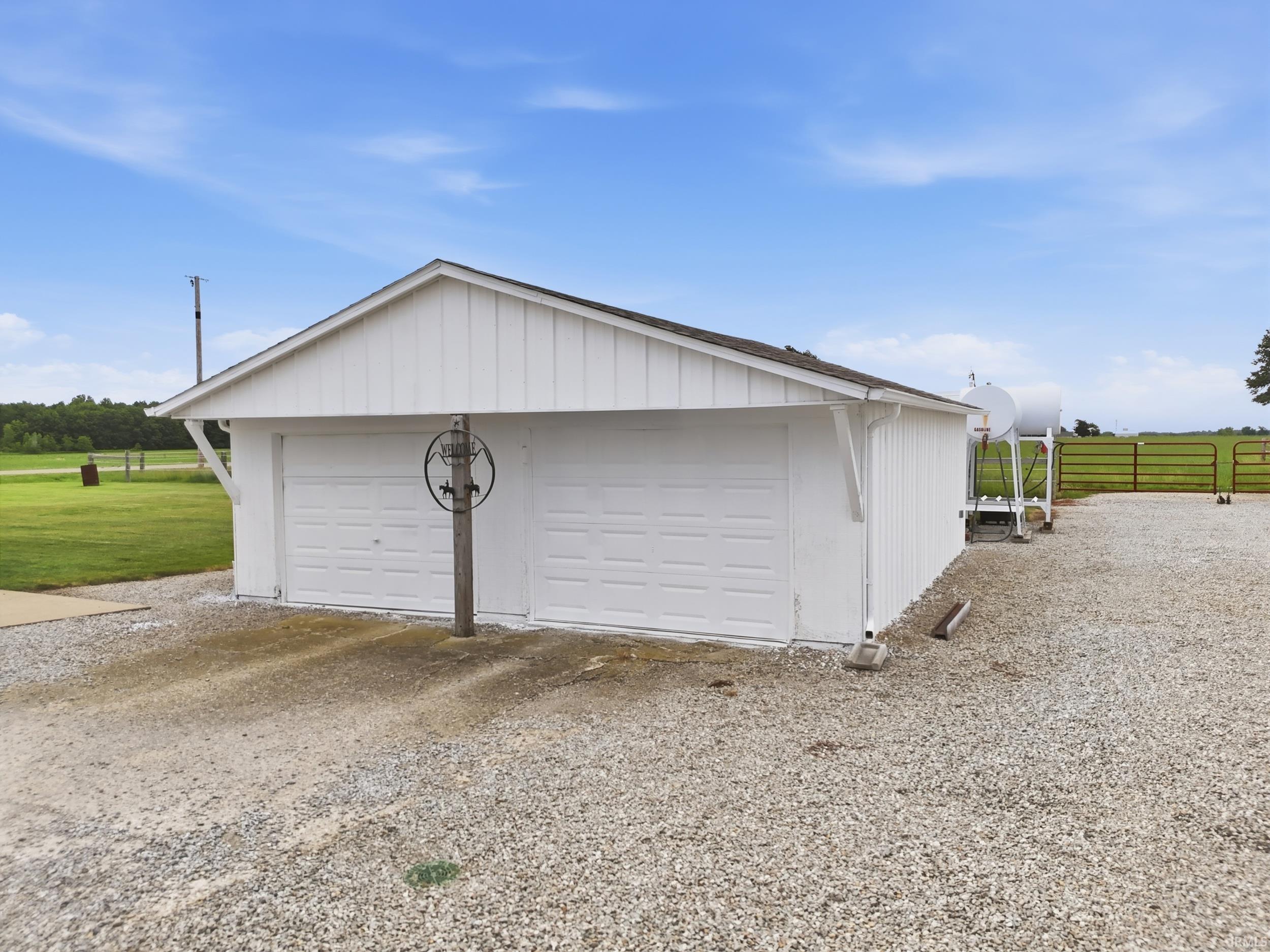 Detached two-car garage featuring white board and batten siding, dual panel garage doors, and a gravel driveway