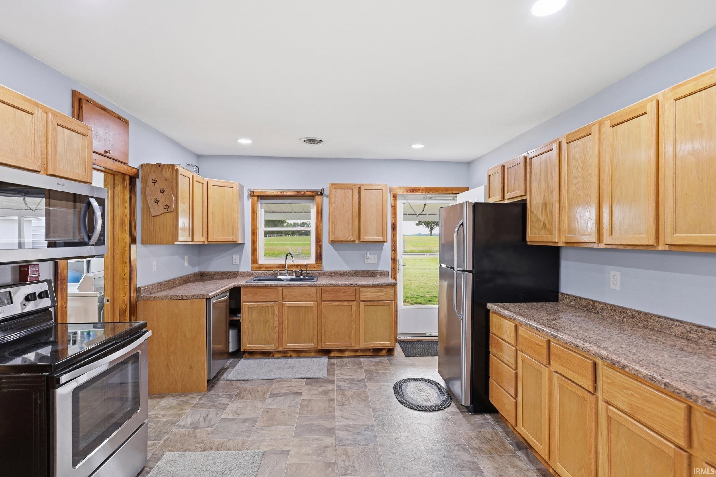 Kitchen featuring wood-finish cabinetry, solid surface countertops, and stainless steel appliances including a range, microwave, and refrigerator