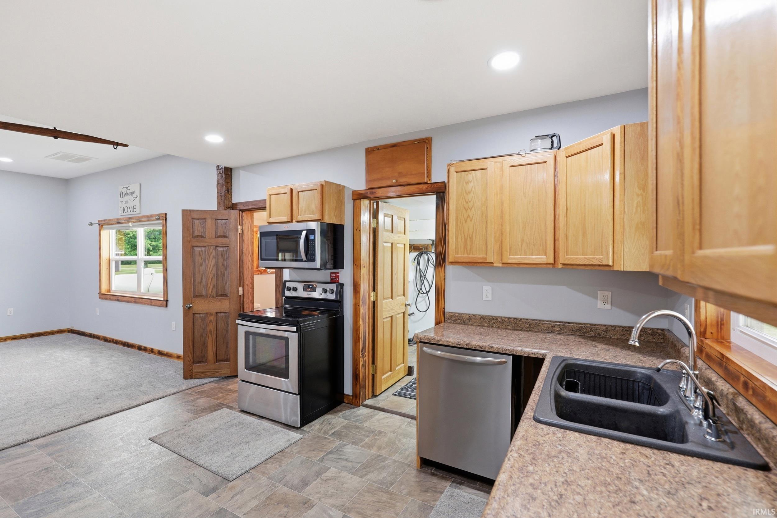 Kitchen area featuring wood-finish cabinetry, a black composite sink, and a stainless steel dishwasher