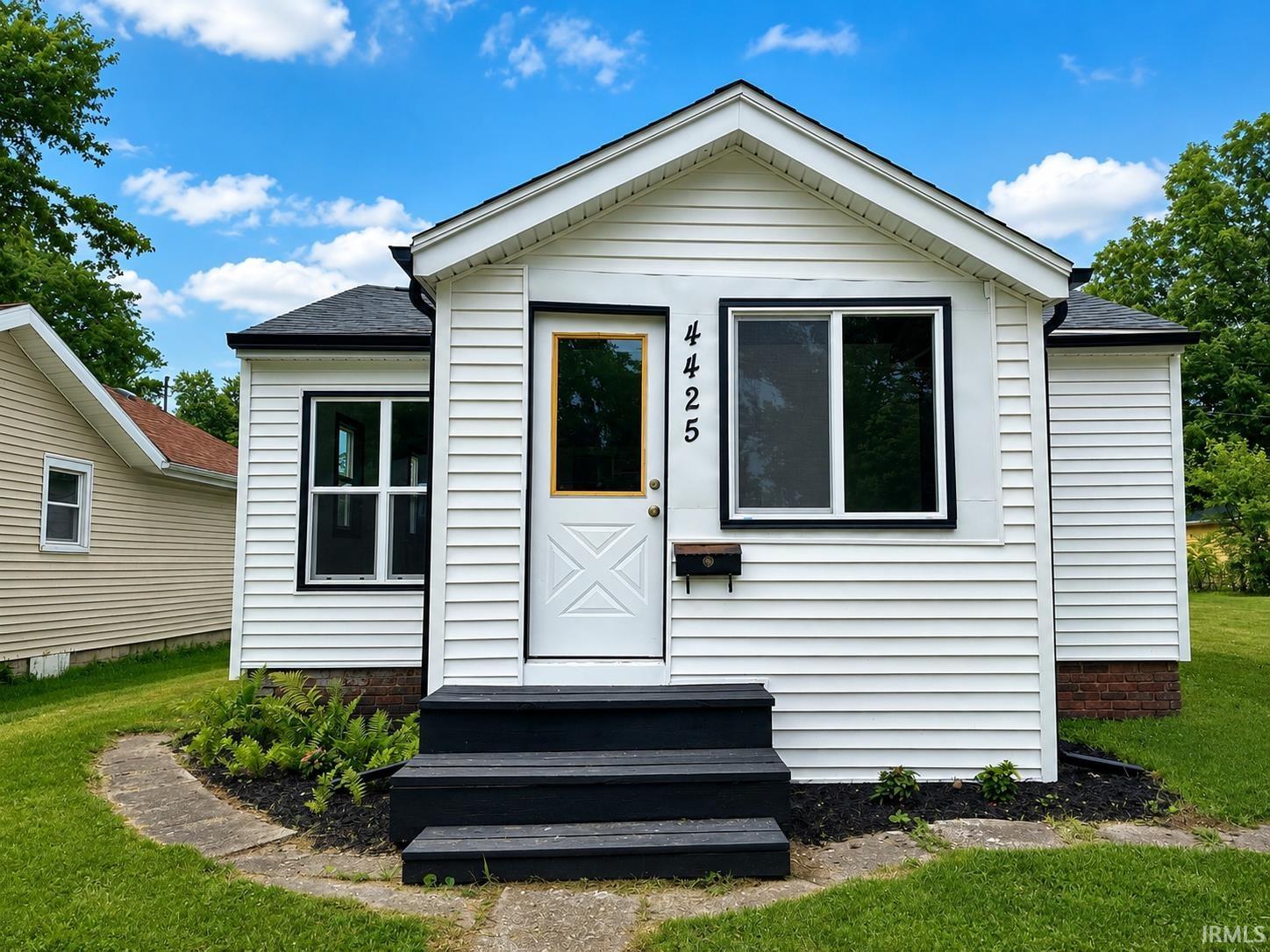 White siding exterior with black trim windows, a white entry door with a wood-finish frame, and black painted steps