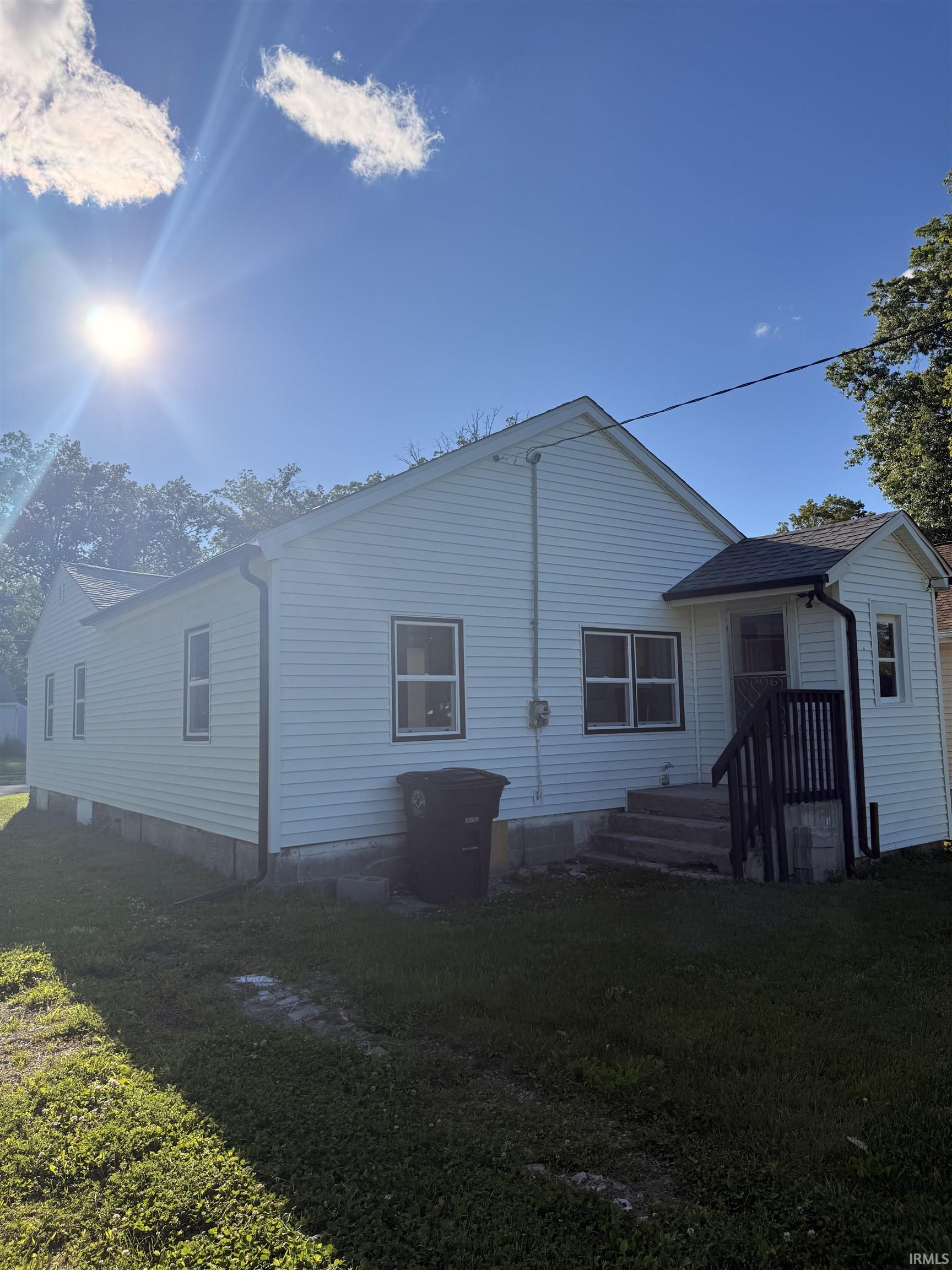 White vinyl siding exterior with multiple windows and a rear entry featuring a dark-stained railing and concrete steps